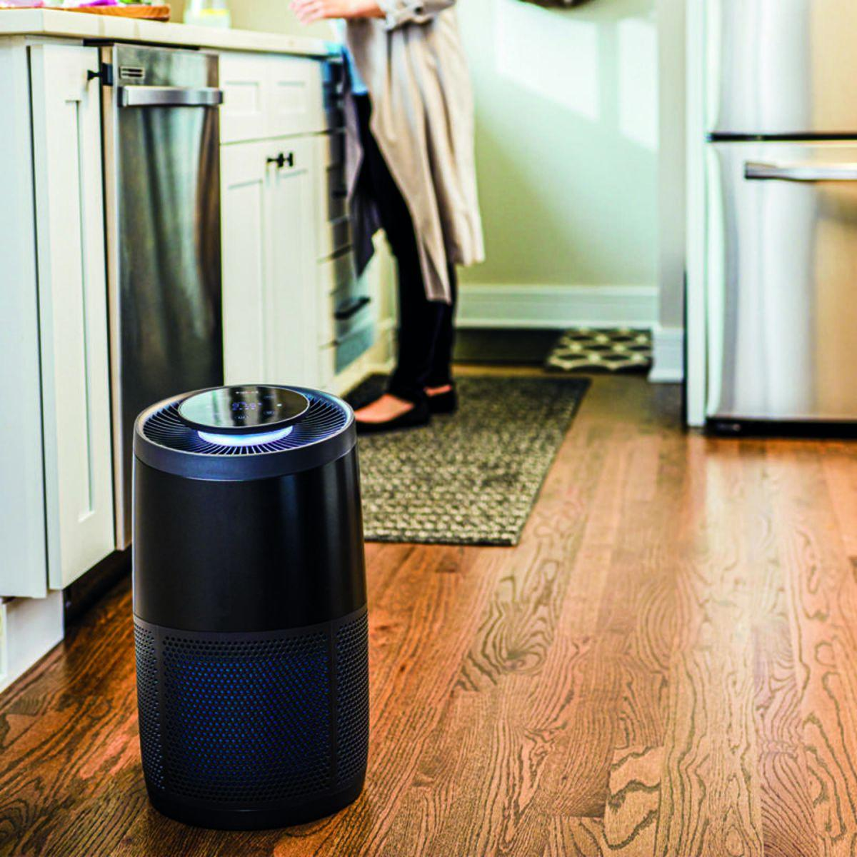 Un purificatore d'aria con una persona sullo sfondo in una cucina con pavimenti in legno.