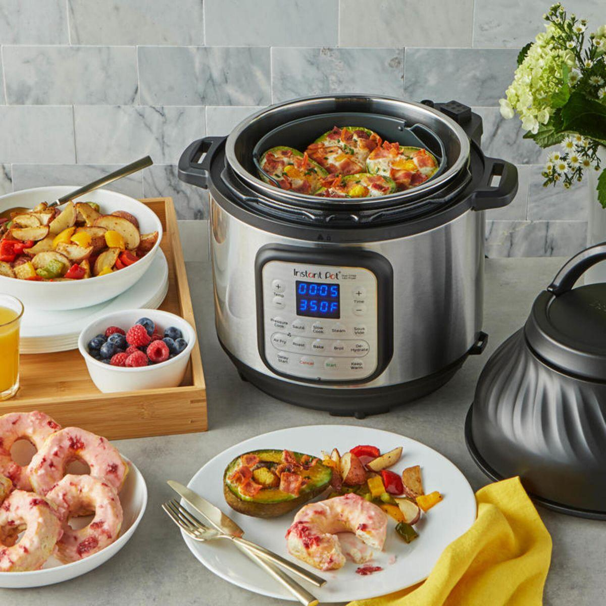 Una Instant Pot con cibo all'interno, circondata da piatti di cibo. Un vassoio di bacche e succo è a sinistra.