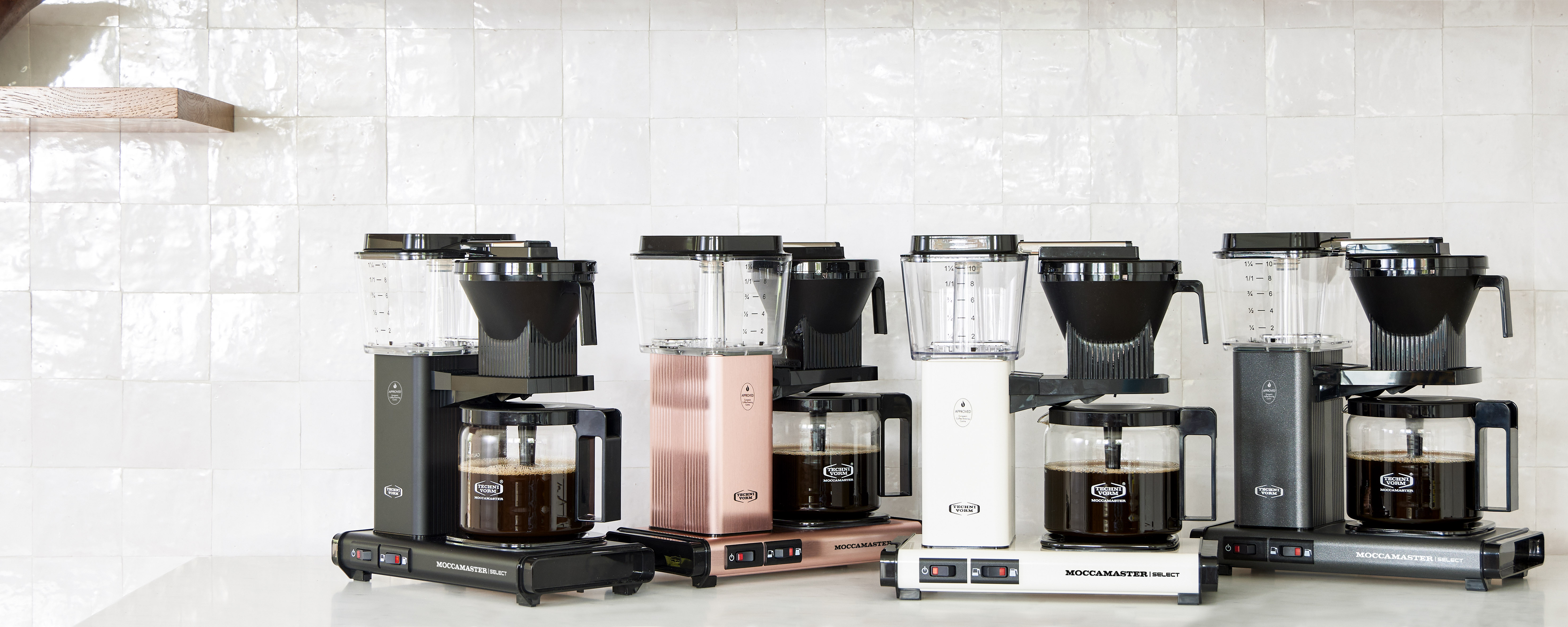 Kilka ekspresów do kawy w rzędzie. Są w różnych kolorach i mają szklane karafki.