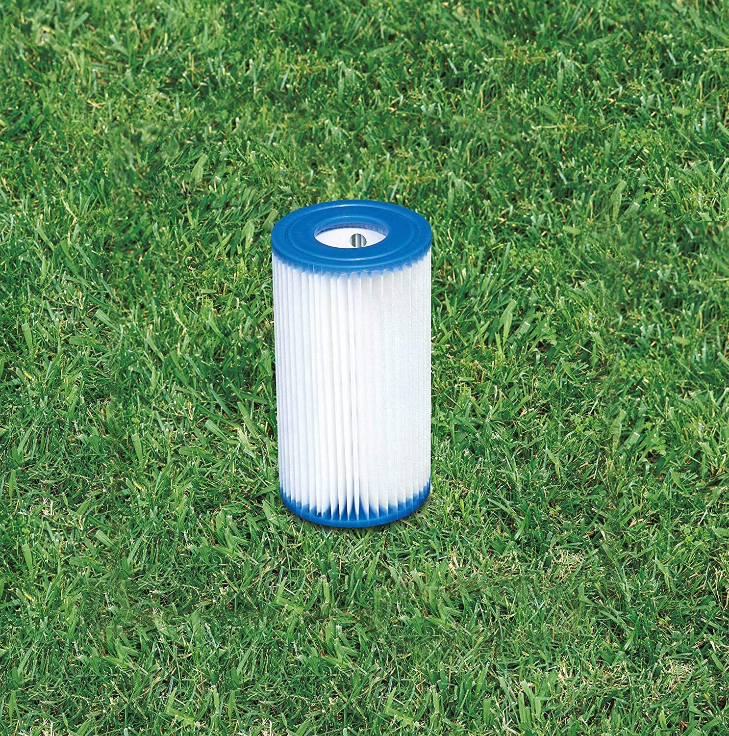 Ein zylindrischer Filter mit weißem, plissiertem Material und blauen Rändern, auf grünem Gras.