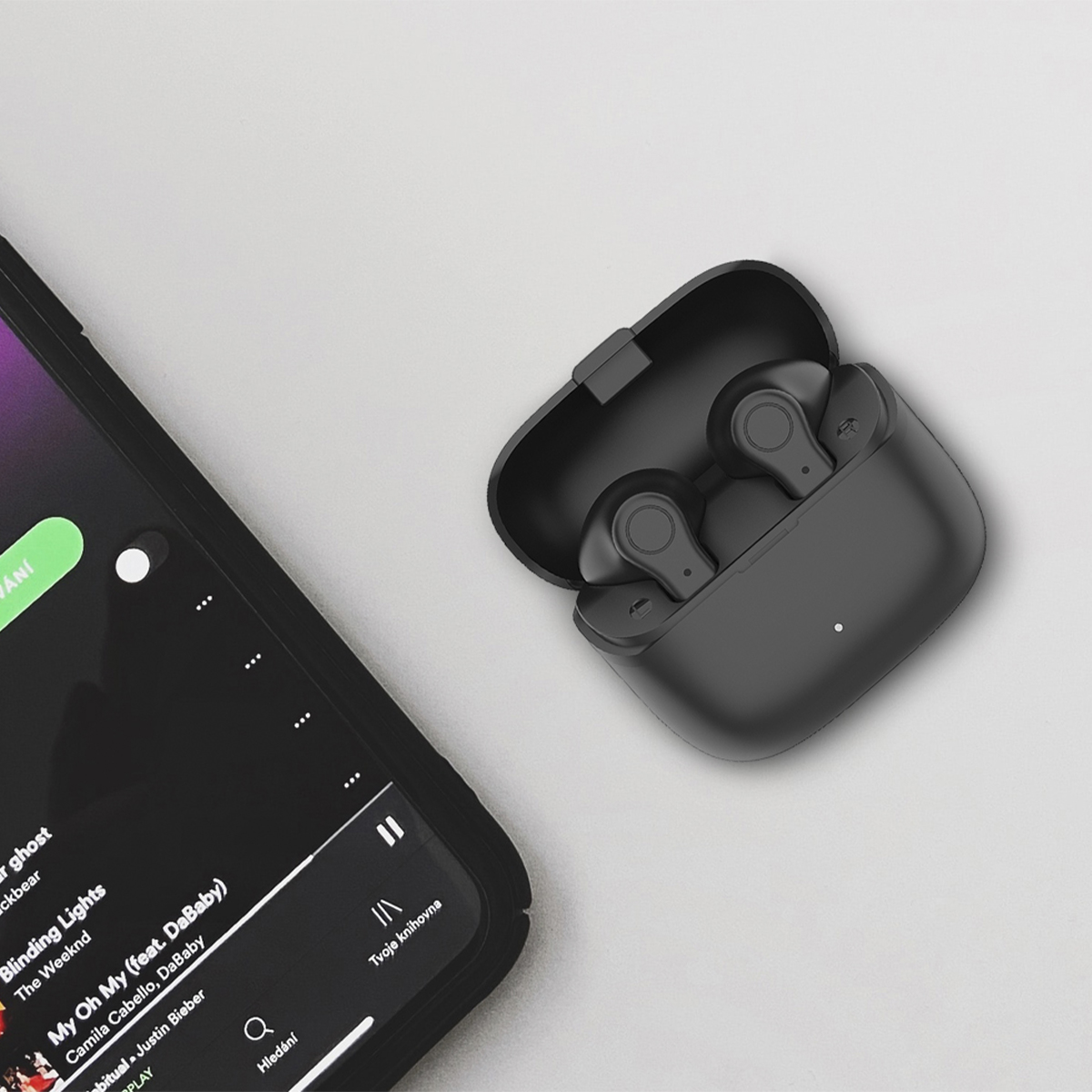 Schwarze Ohrhörer im Etui, neben einem Telefon, das eine Musik-App mit The Weeknd anzeigt.