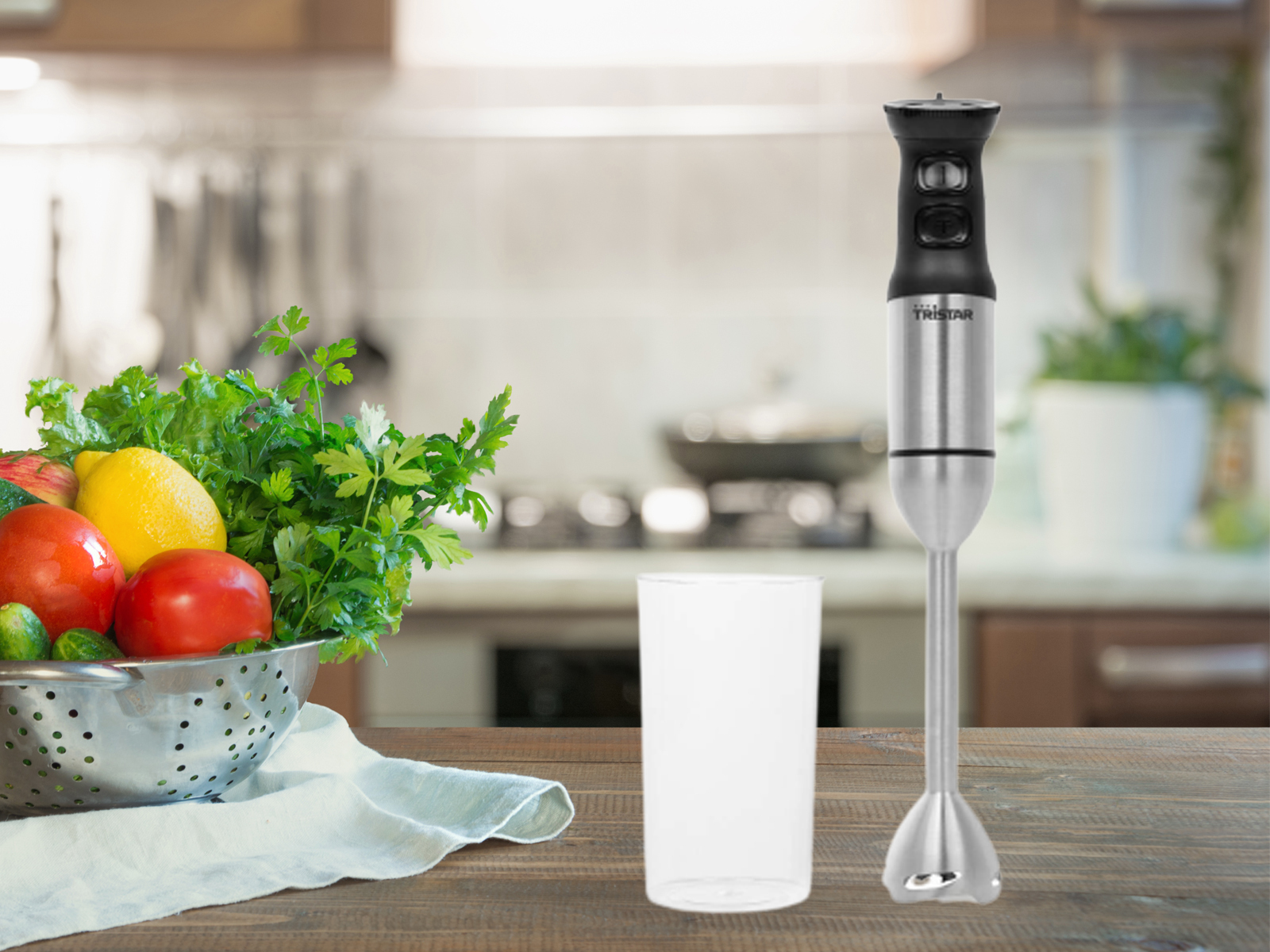 Blender ręczny, owoce, warzywa w metalowej misce i szklanka na drewnianym stole w kuchni.