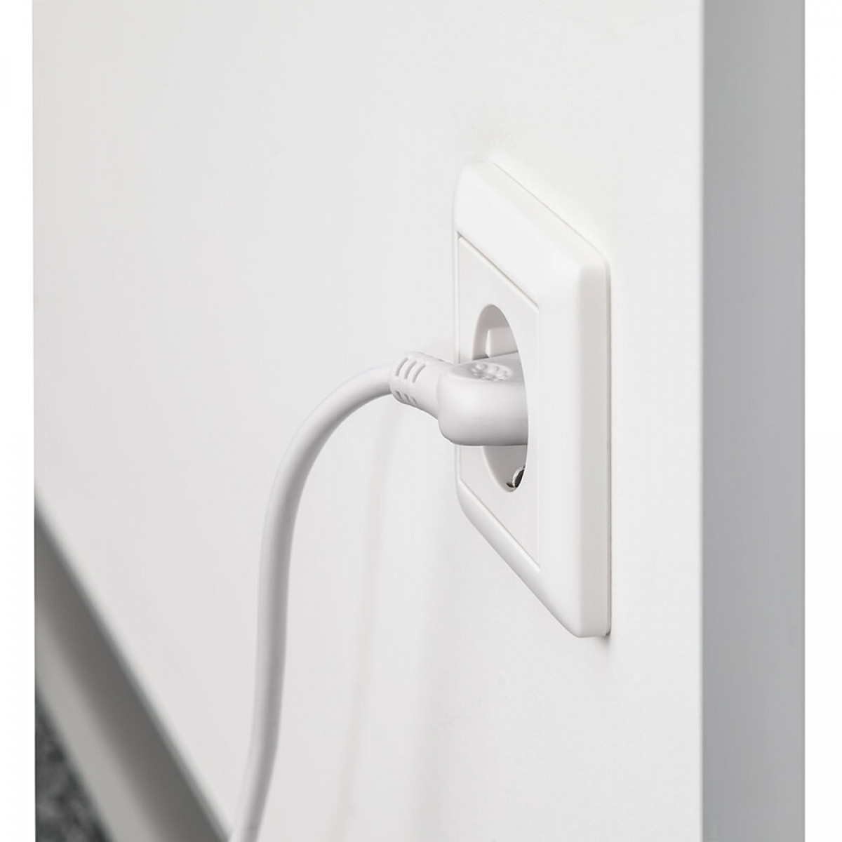 Weiße Steckdose mit eingestecktem weißen Stecker. Die Steckdose befindet sich an einer weißen Wand.