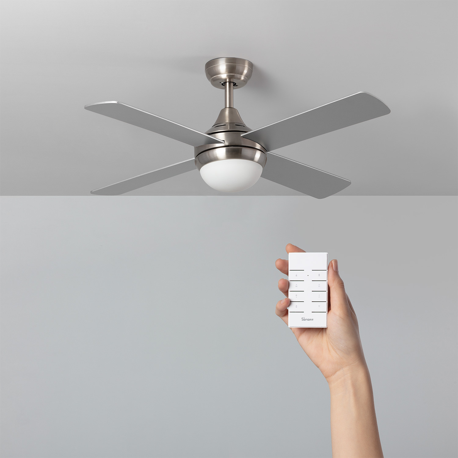 Ventilatore a soffitto con quattro pale e telecomando in mano.