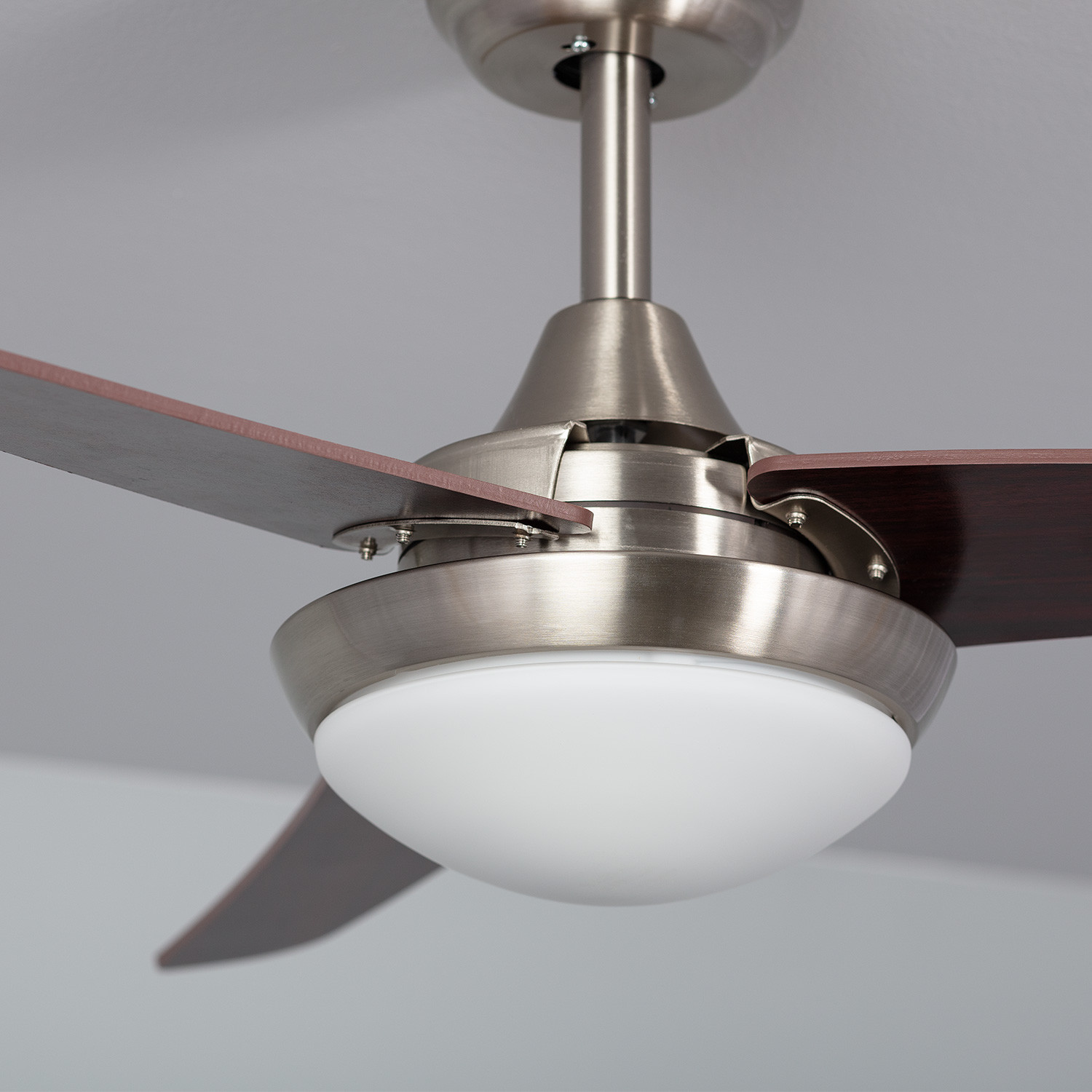 Primo piano di un ventilatore a soffitto con pale in legno scuro e un apparecchio di illuminazione bianco.