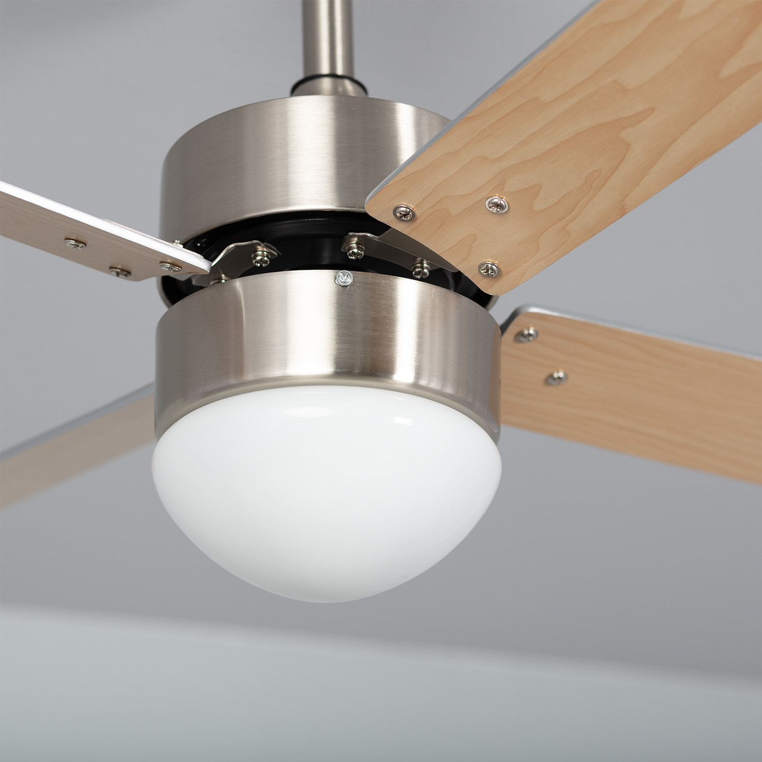 Primo piano di un ventilatore da soffitto. Ha un alloggiamento in metallo, pale in legno chiaro e una luce bianca.