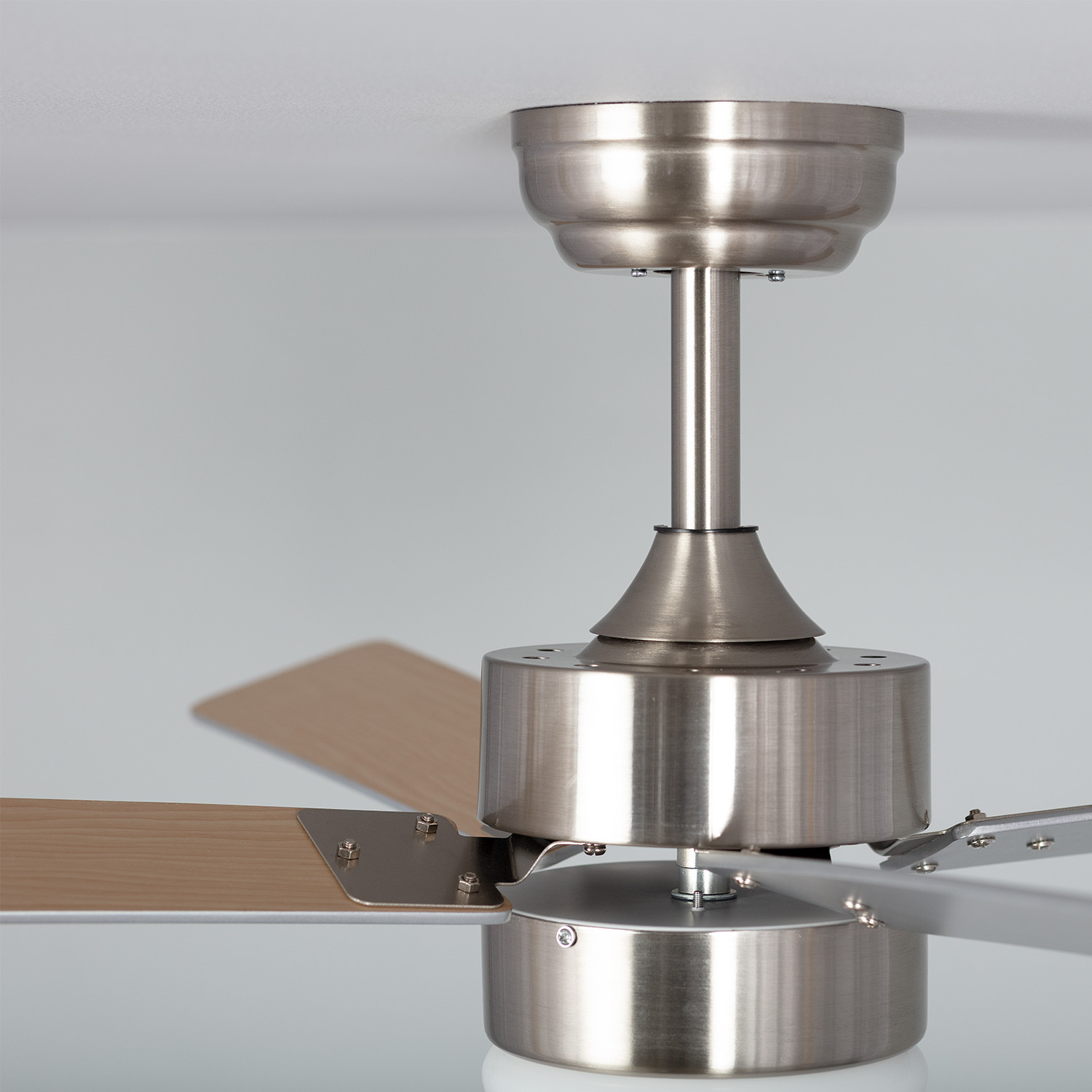 Ventilatore a soffitto con finitura argentata e pale in legno. Le pale sono di colore marrone chiaro.