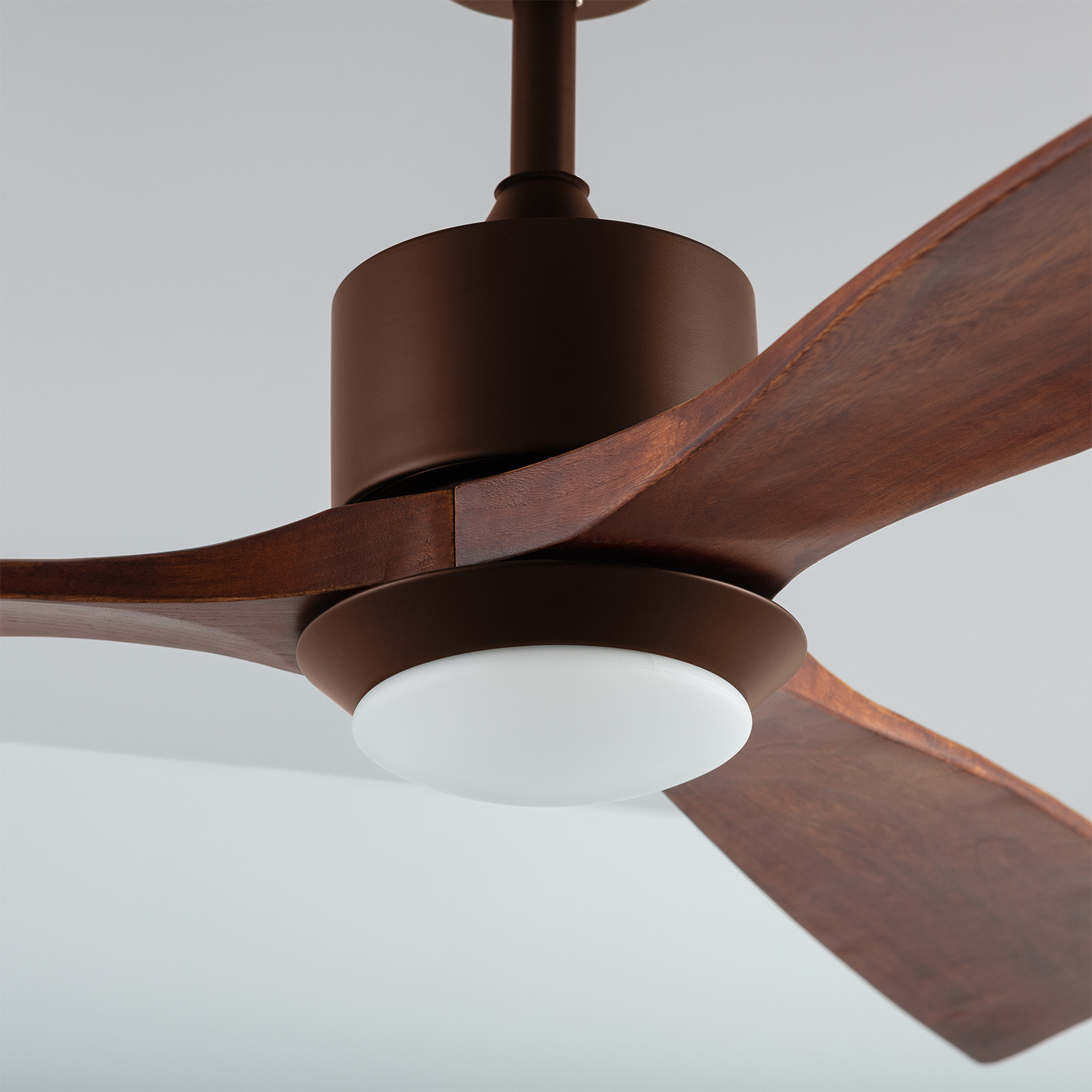 Un ventilatore da soffitto marrone con pale in legno e un apparecchio di illuminazione in un soffitto bianco.