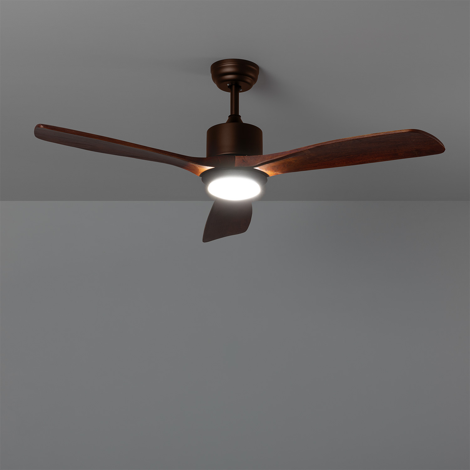 Un ventilatore da soffitto marrone con tre pale e un'apparecchio di illuminazione centrale montato su un soffitto grigio.