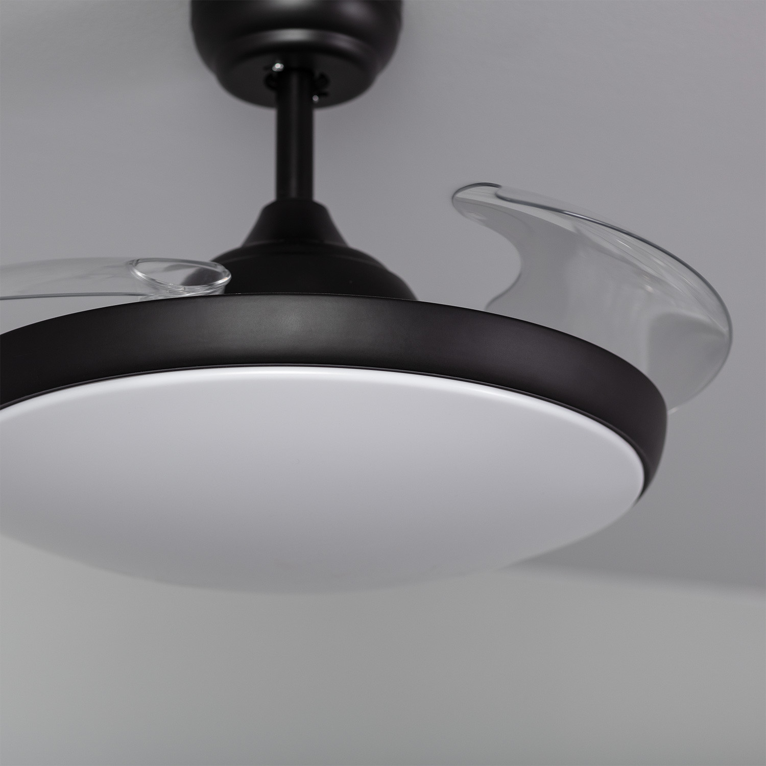 Primo piano di un ventilatore da soffitto nero con pale trasparenti e una luce bianca.