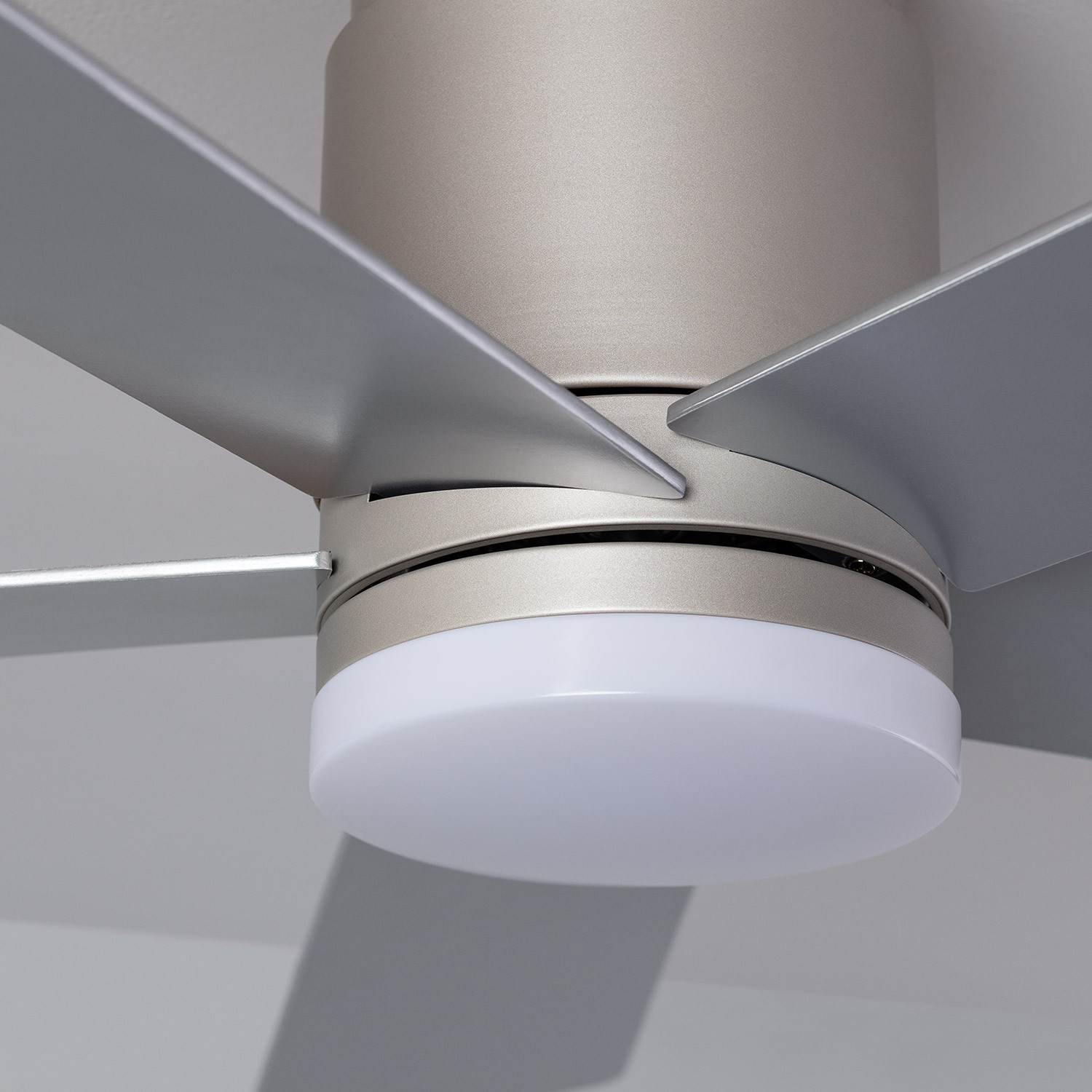 Primo piano di un ventilatore a soffitto, finitura metallica argentata, con luce circolare illuminata e pale.