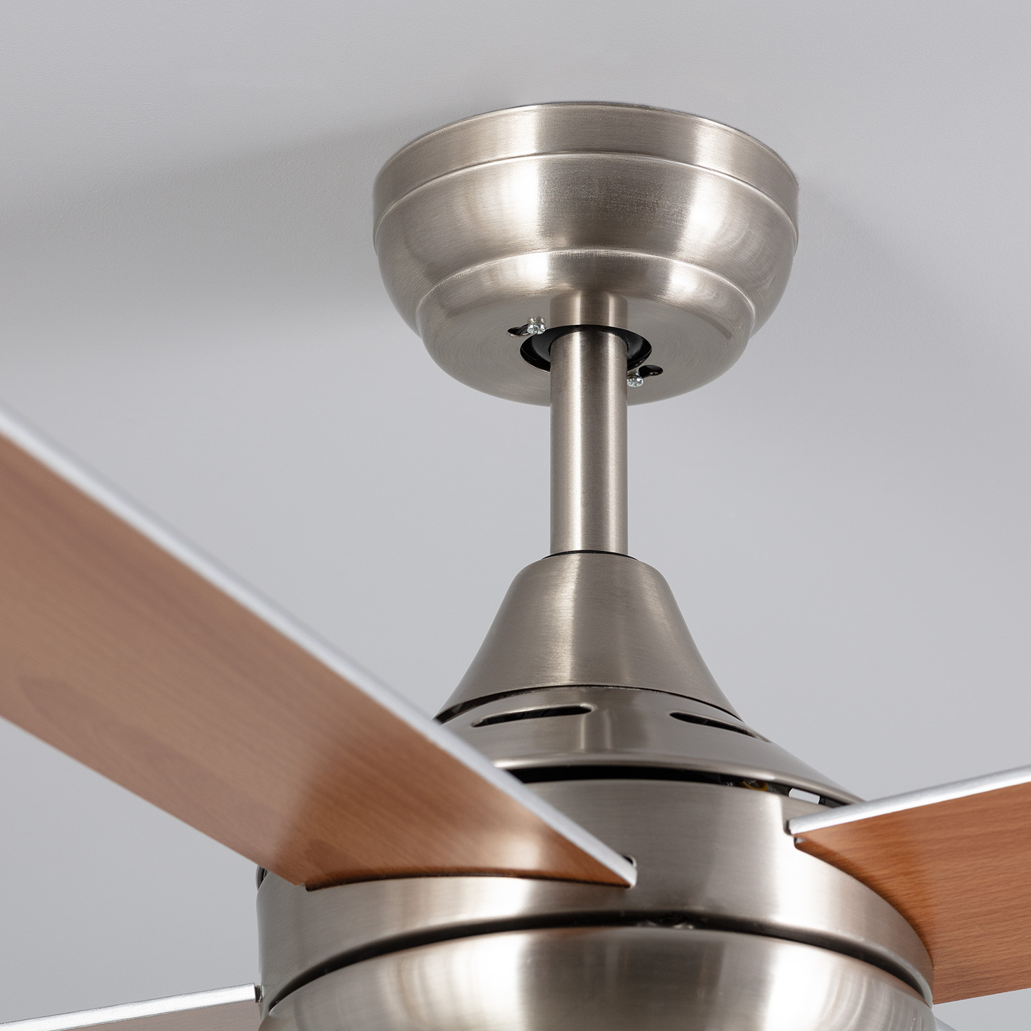 Primo piano di un ventilatore a soffitto che mostra pale e fissaggio, con soffitto bianco.