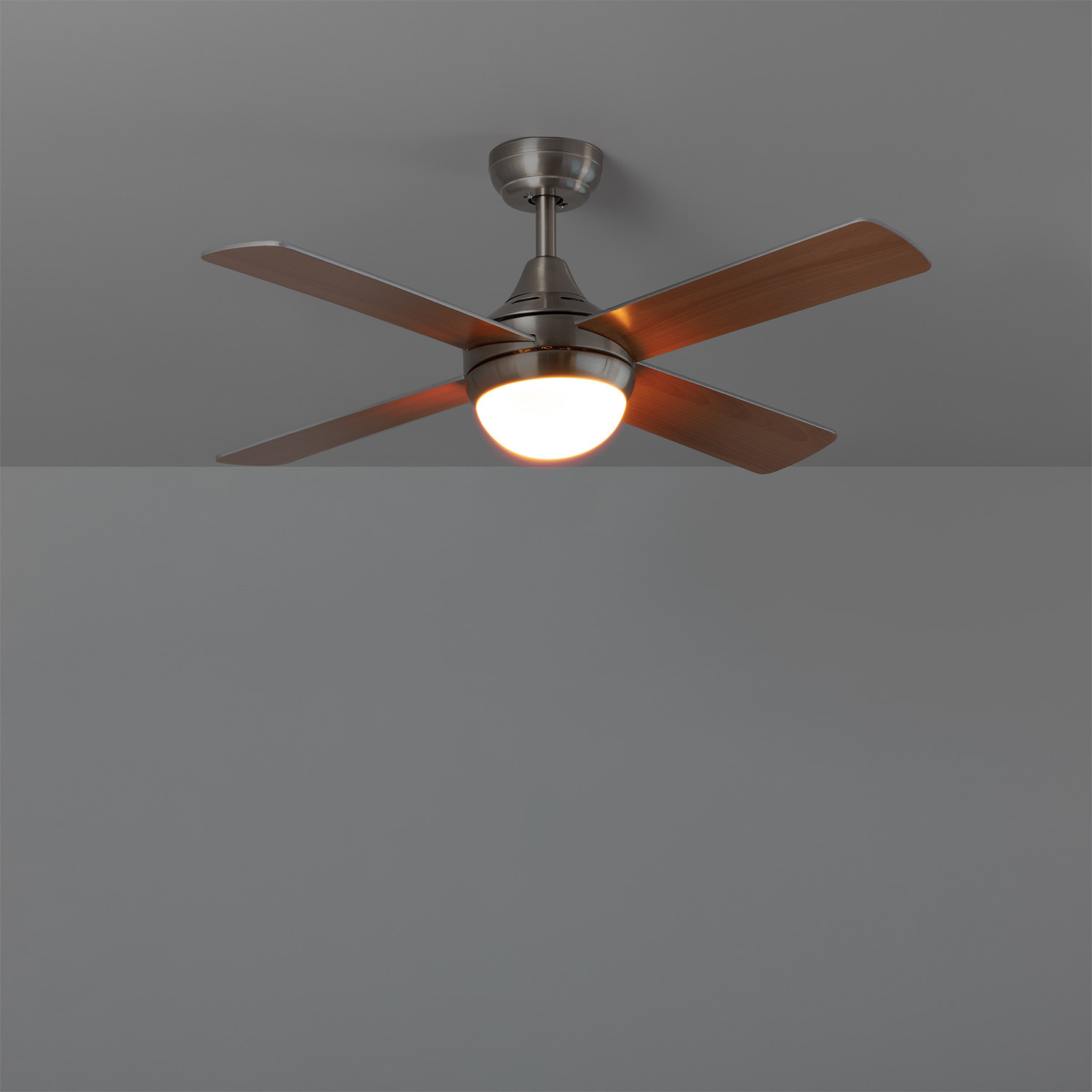 Un ventilatore da soffitto con pale in legno, illuminato con una luce calda, su sfondo grigio.
