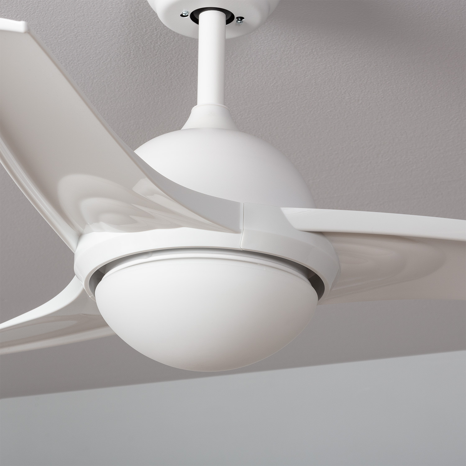 Ventilatore da soffitto bianco a tre pale, centrato su un soffitto bianco. Illuminato da luce bianca.