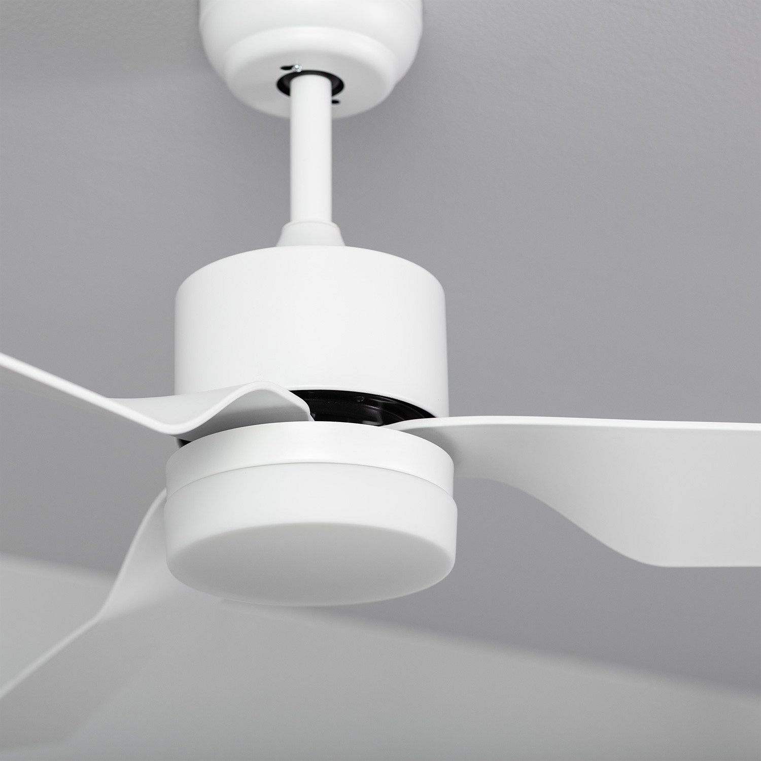 Un primo piano del motore e delle pale di un ventilatore da soffitto bianco su sfondo grigio.
