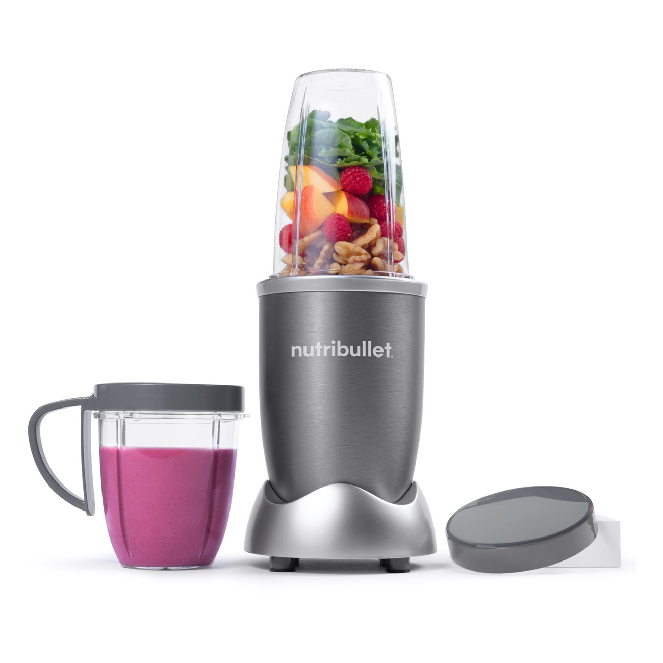Mixer mit Obst und Gemüse. Links ein Becher mit rosa Smoothie.