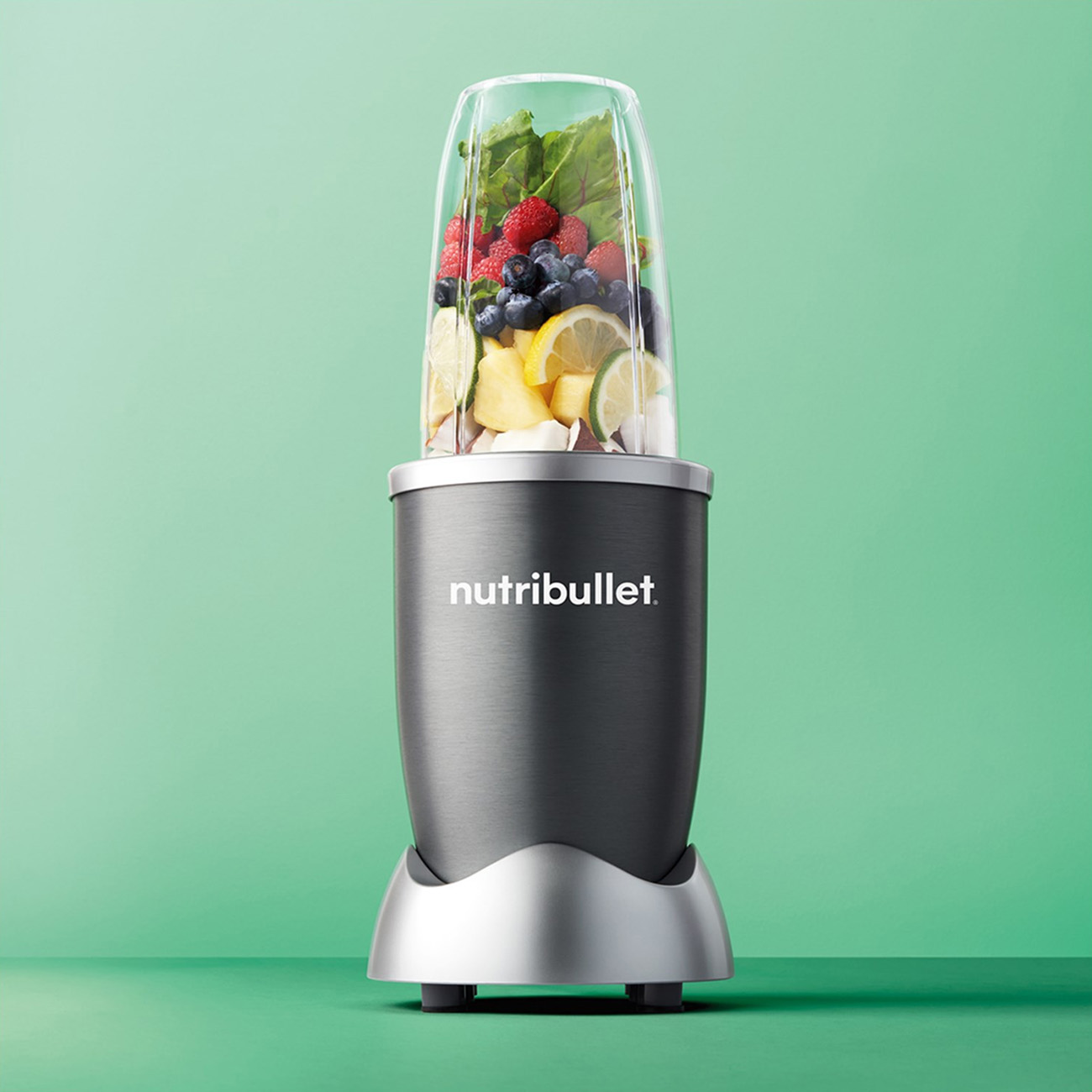 Nutribullet-Mixer mit Früchten und Gemüse. Grüner Hintergrund.