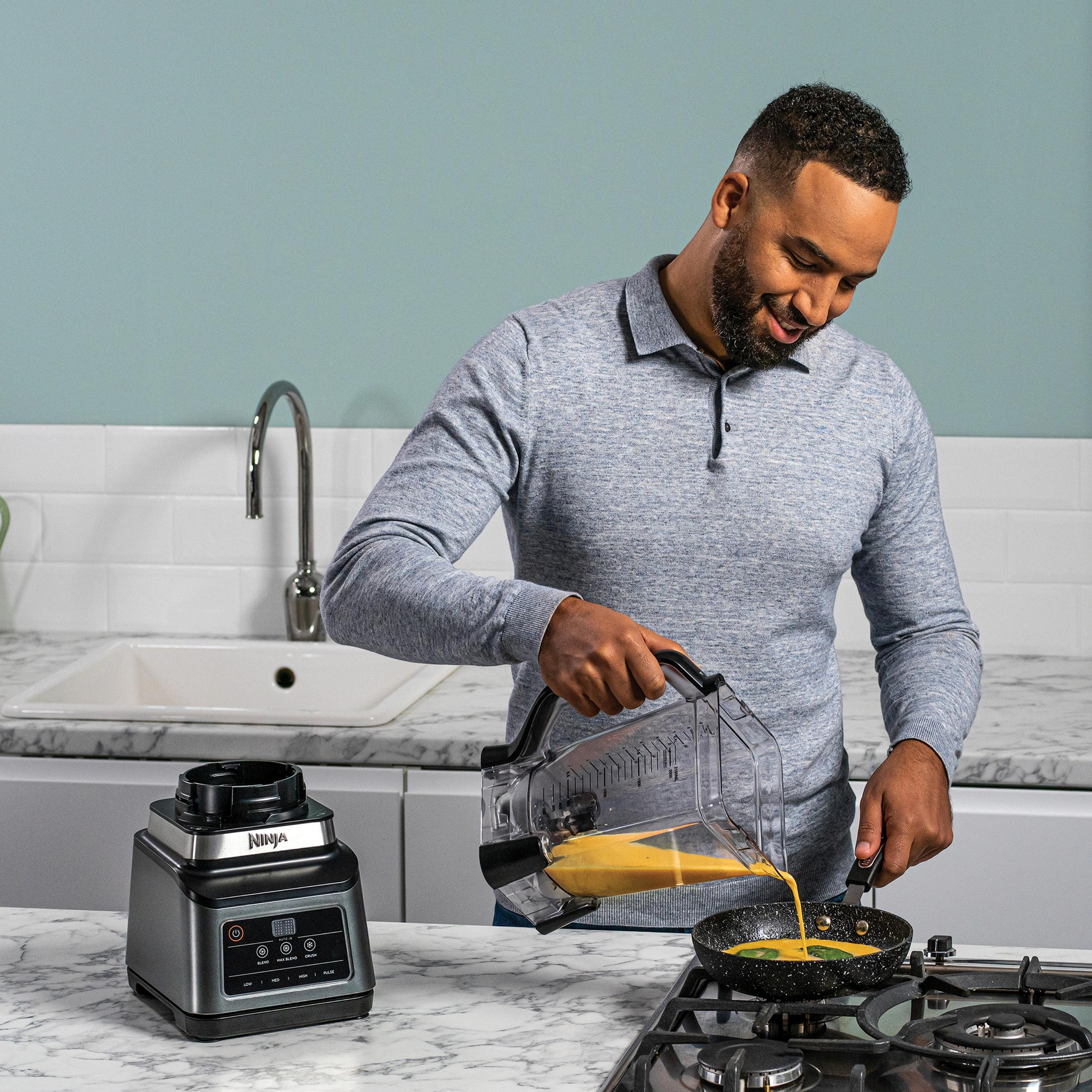 Mężczyzna wlewa płyn z blendera do patelni. Otoczenie kuchni z marmurowym blatem.