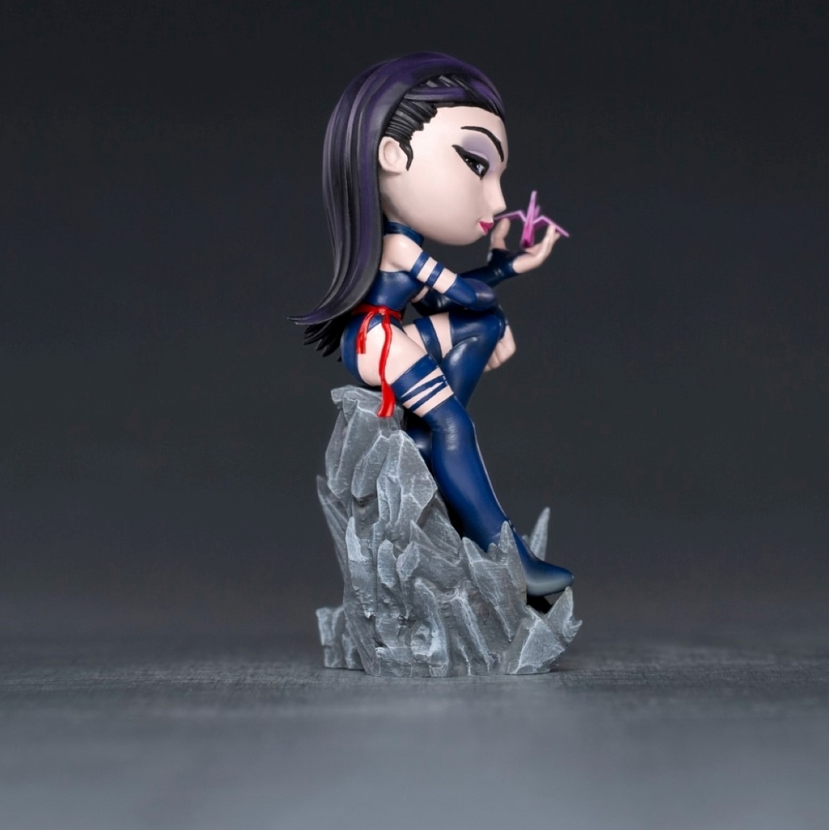 Psylocke-Figur, sitzt auf einem Felsen, hält ein Psychomesser, dunkler Hintergrund.