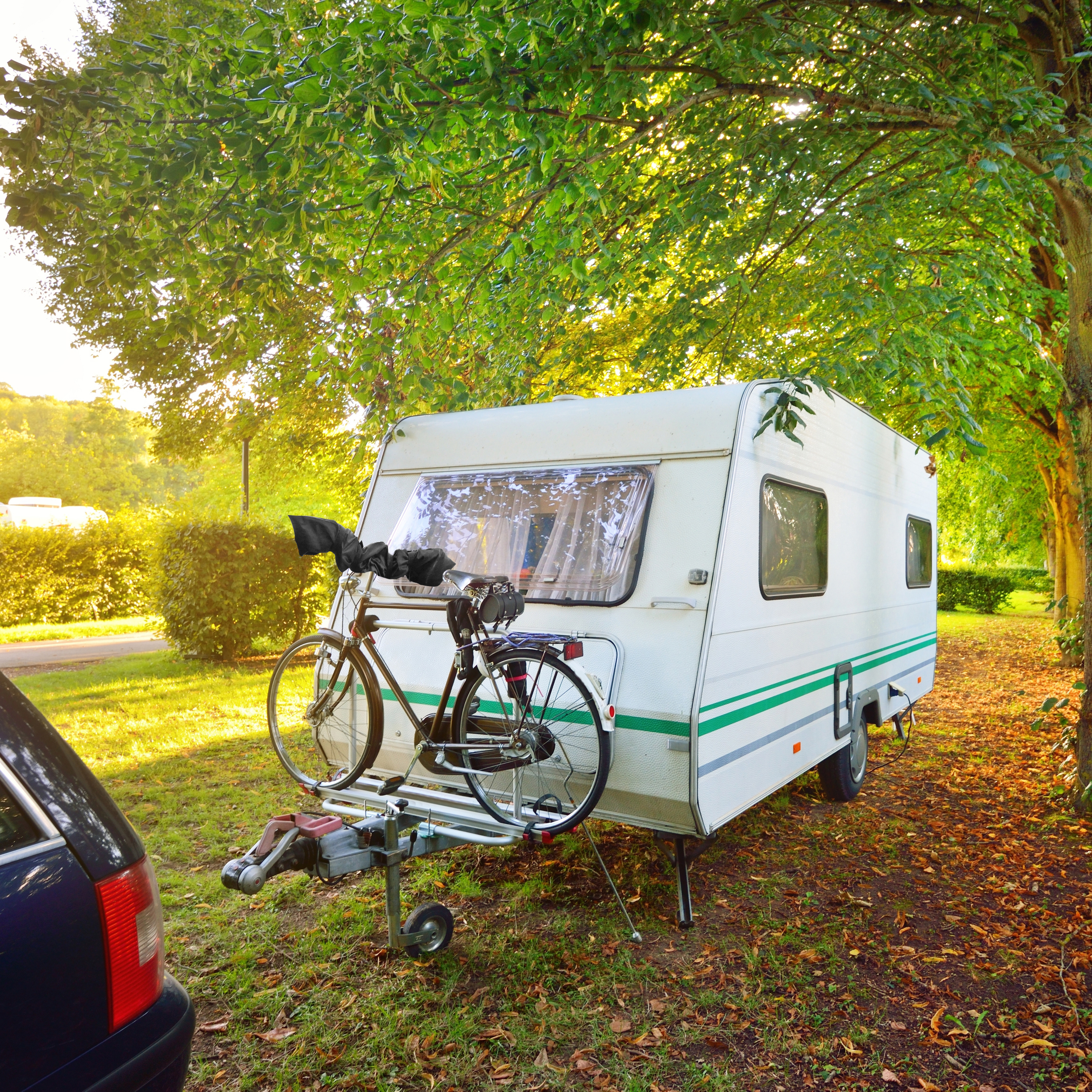 Weißer Wohnwagen mit schwarzem Fahrradträger, geparkt auf Gras in der Nähe von Bäumen.