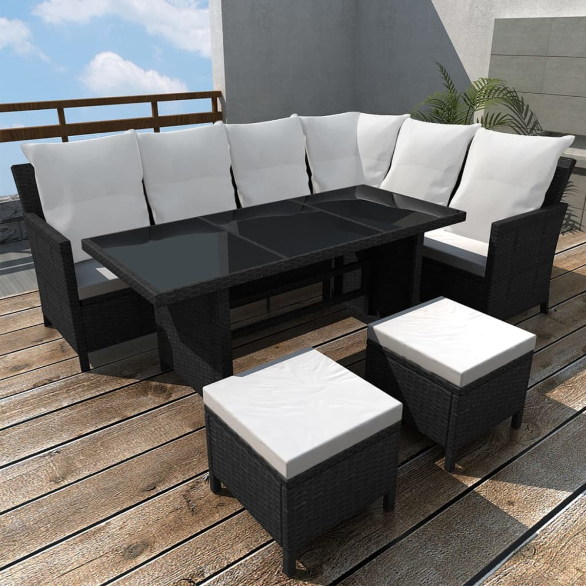 Schwarzes Korbmöbel-Set mit weißen Kissen und einem schwarzen Tisch auf einer Terrasse.