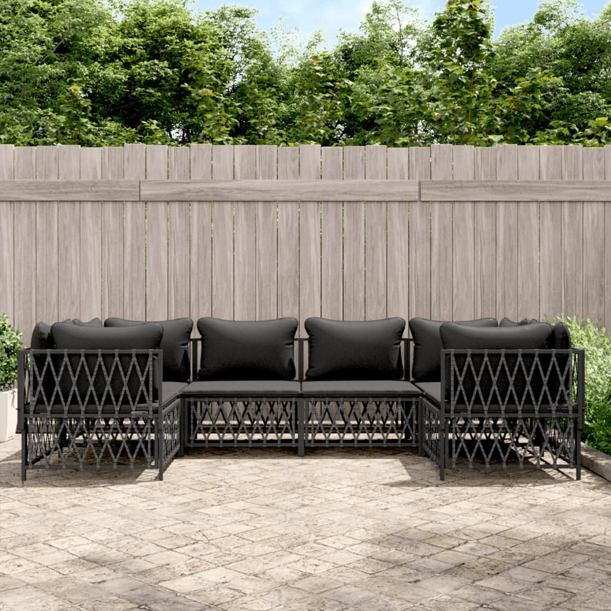 Schwarzes Outdoor-Sofaset auf einer Backstein-Terrasse, Holzzaun, grüne Bäume im Hintergrund.