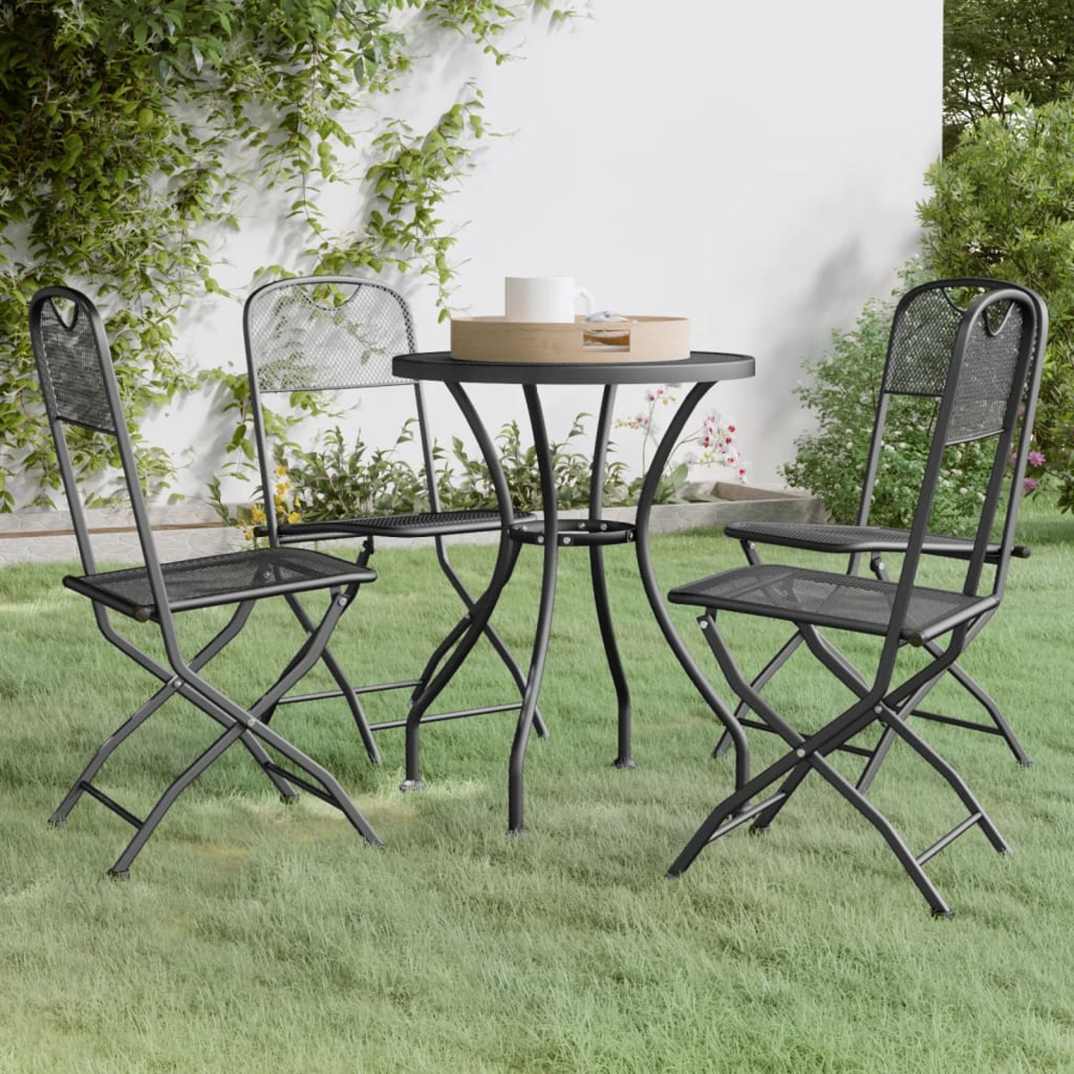 Ein schwarzes Metall Tisch- und Stuhlset auf Gras. Ein Tablett mit einer Tasse steht auf dem Tisch.