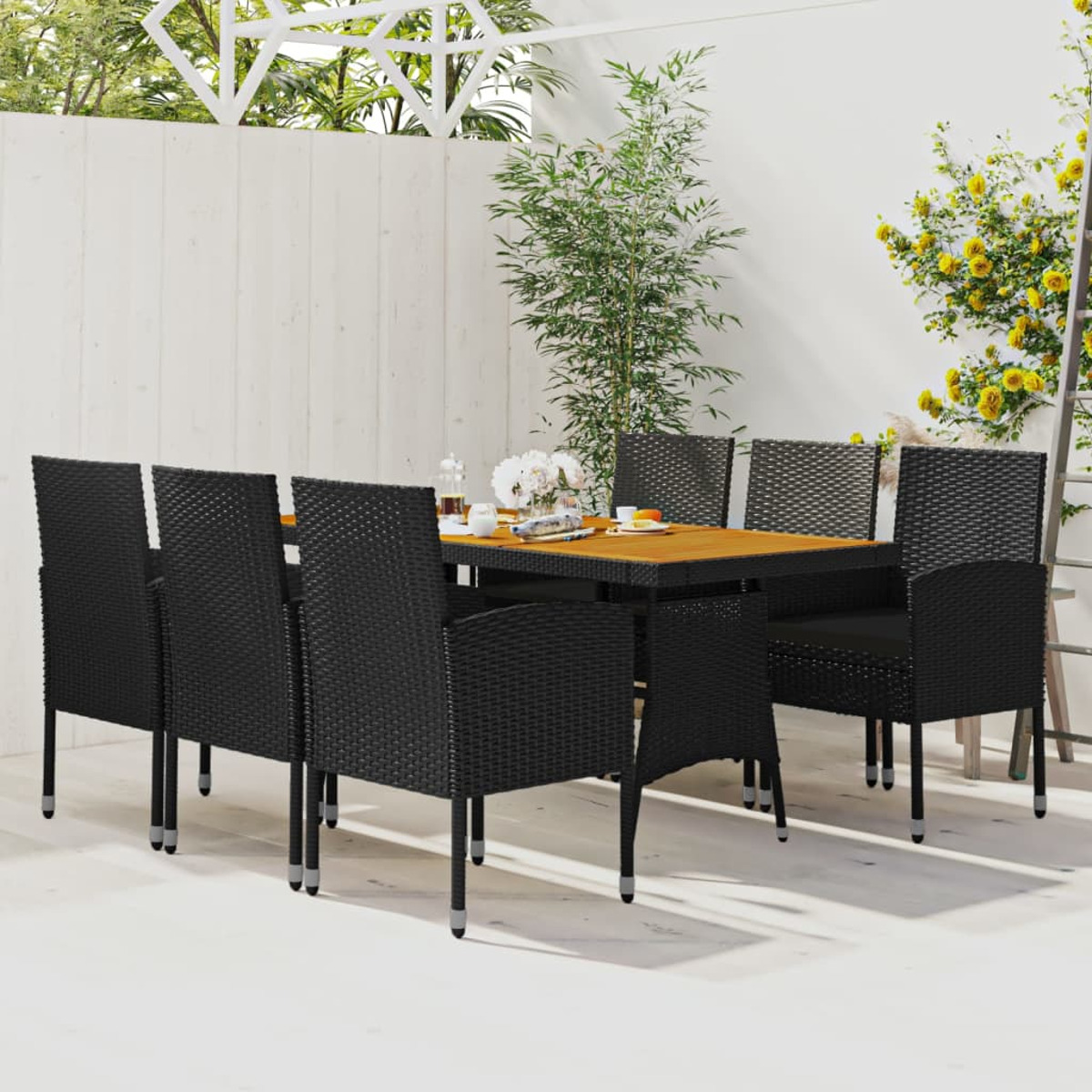 Essgruppe für den Außenbereich mit schwarzen Korbstühlen und einem Holztisch, weißer Wandhintergrund.