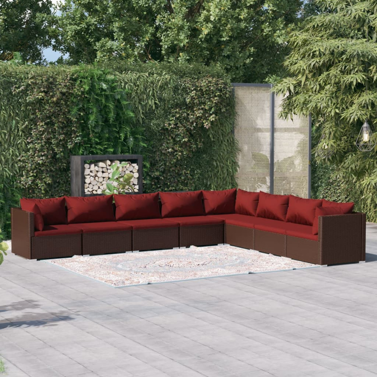 Braunes, gewebtes Outdoor-Sofagarnitur mit roten Kissen. Enthält Sofa, Teppich und grünen Hintergrund.