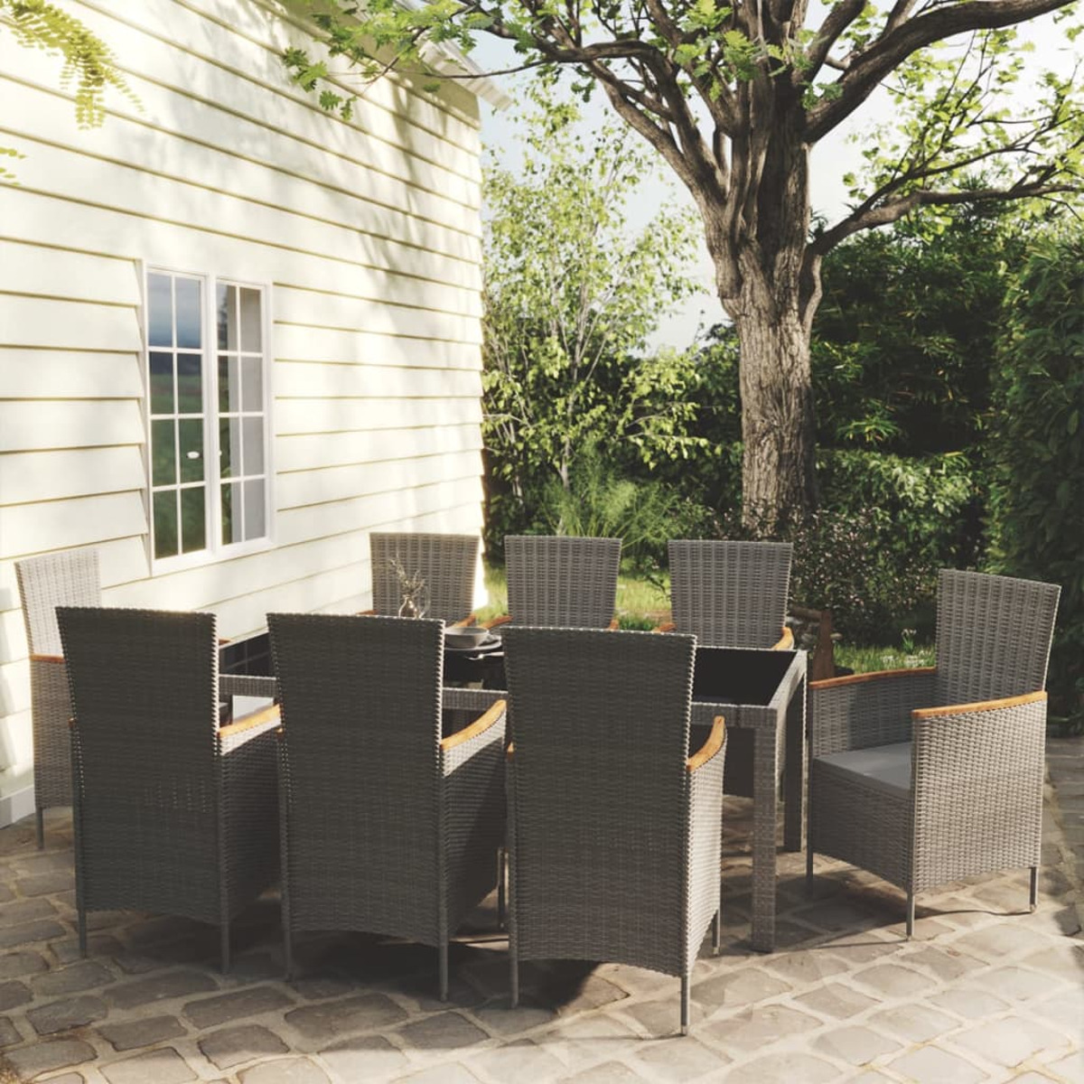 Essgruppe im Freien mit grauen Korbstühlen und einem Tisch mit Glasplatte auf einer gepflasterten Terrasse.