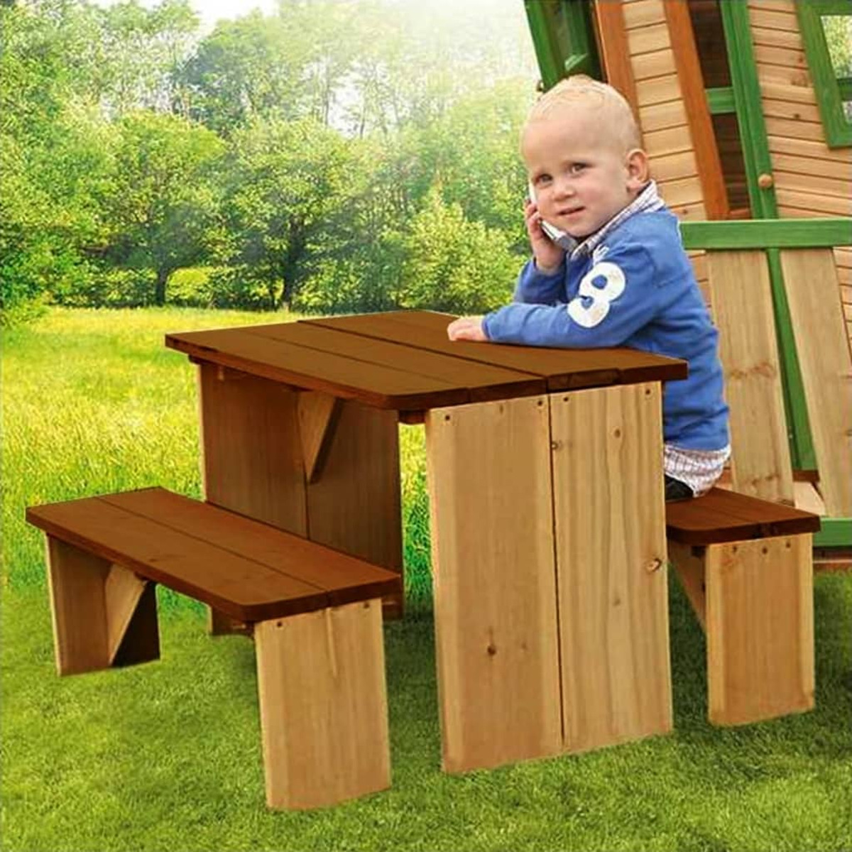 Ein junges Kind sitzt an einem Picknicktisch aus Holz, mit blauem Hemd und braunem Tisch.