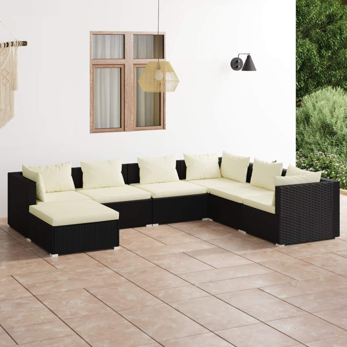Schwarzes Ecksofa aus Korbgeflecht mit cremefarbenen Kissen auf einer gefliesten Terrasse.