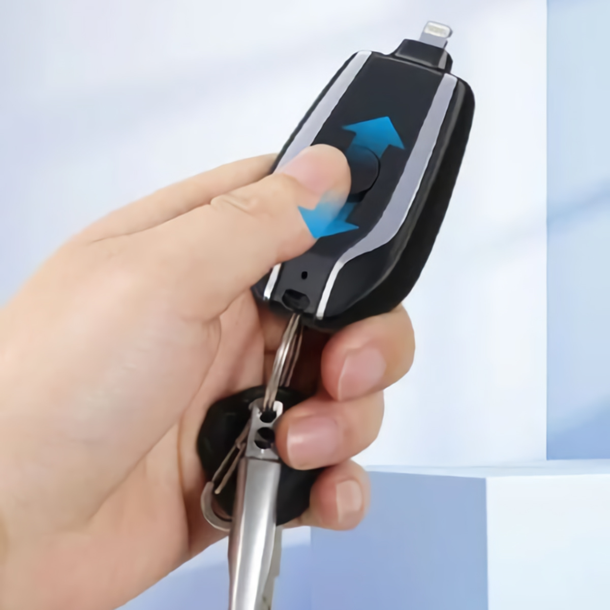 Una mano sosteniendo un dispositivo negro y plateado en forma de llave con un llavero, con flechas azules.