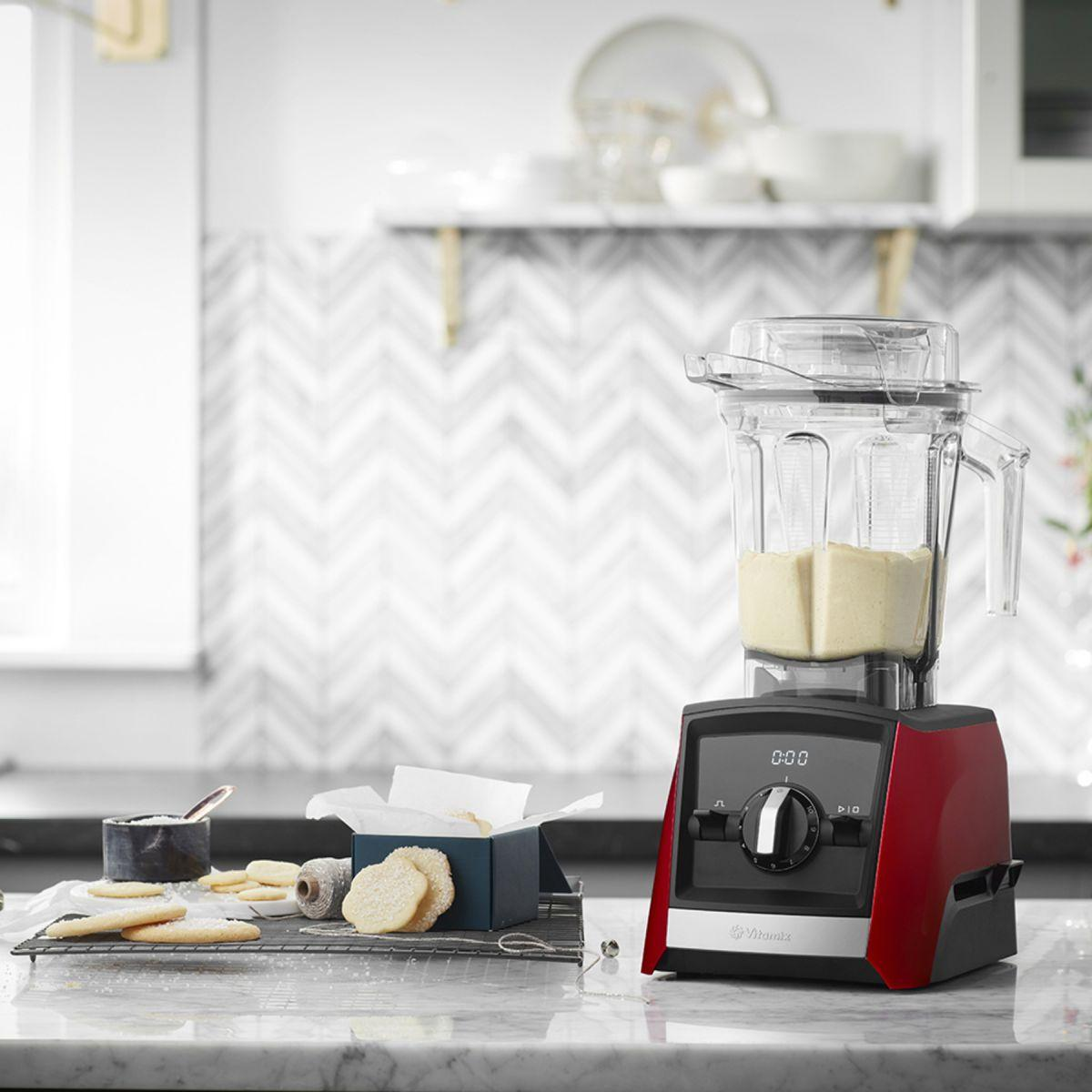 Frullatore con base rossa, biscotti e scatola blu su un piano di marmo in cucina.