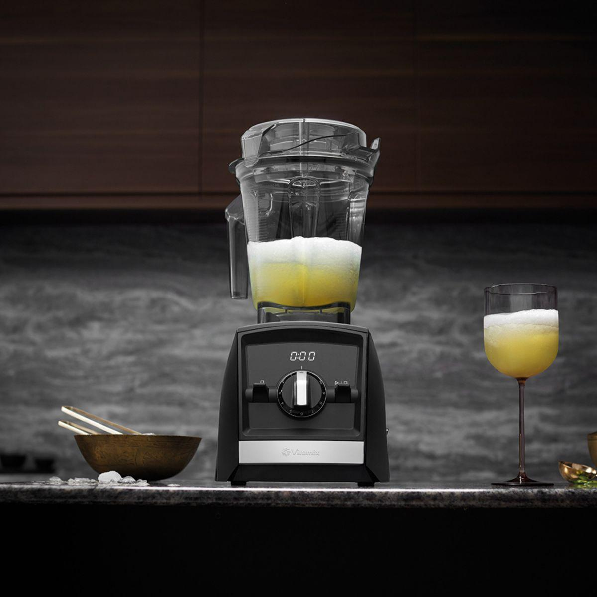 Un frullatore nero con un contenitore trasparente contenente un liquido giallo, accanto a un bicchiere della stessa bevanda.