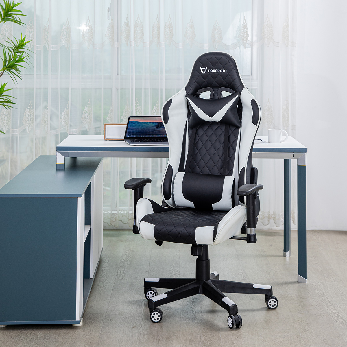 Ein schwarz-weißer Gaming-Stuhl neben einem Schreibtisch mit Laptop und Tasse.