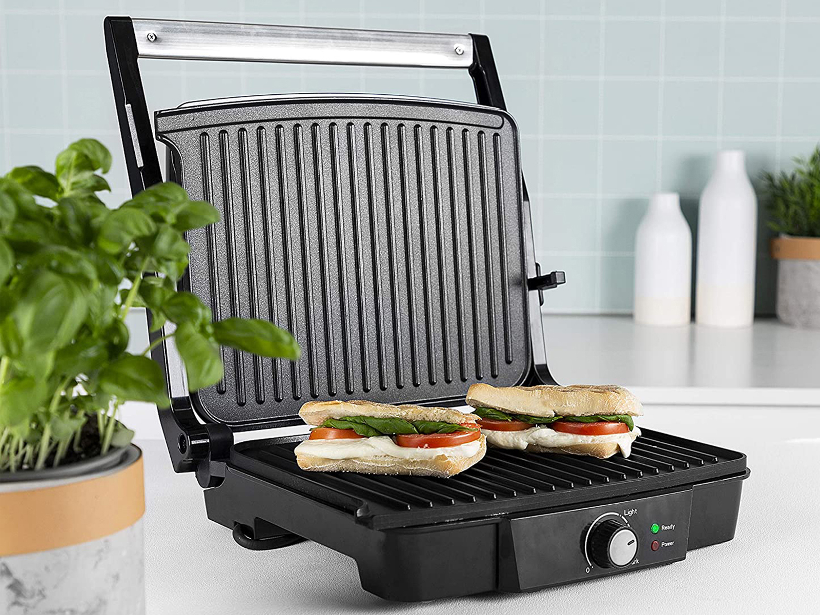 Schwarzer Panini-Grill mit Sandwiches und Basilikumpflanze.