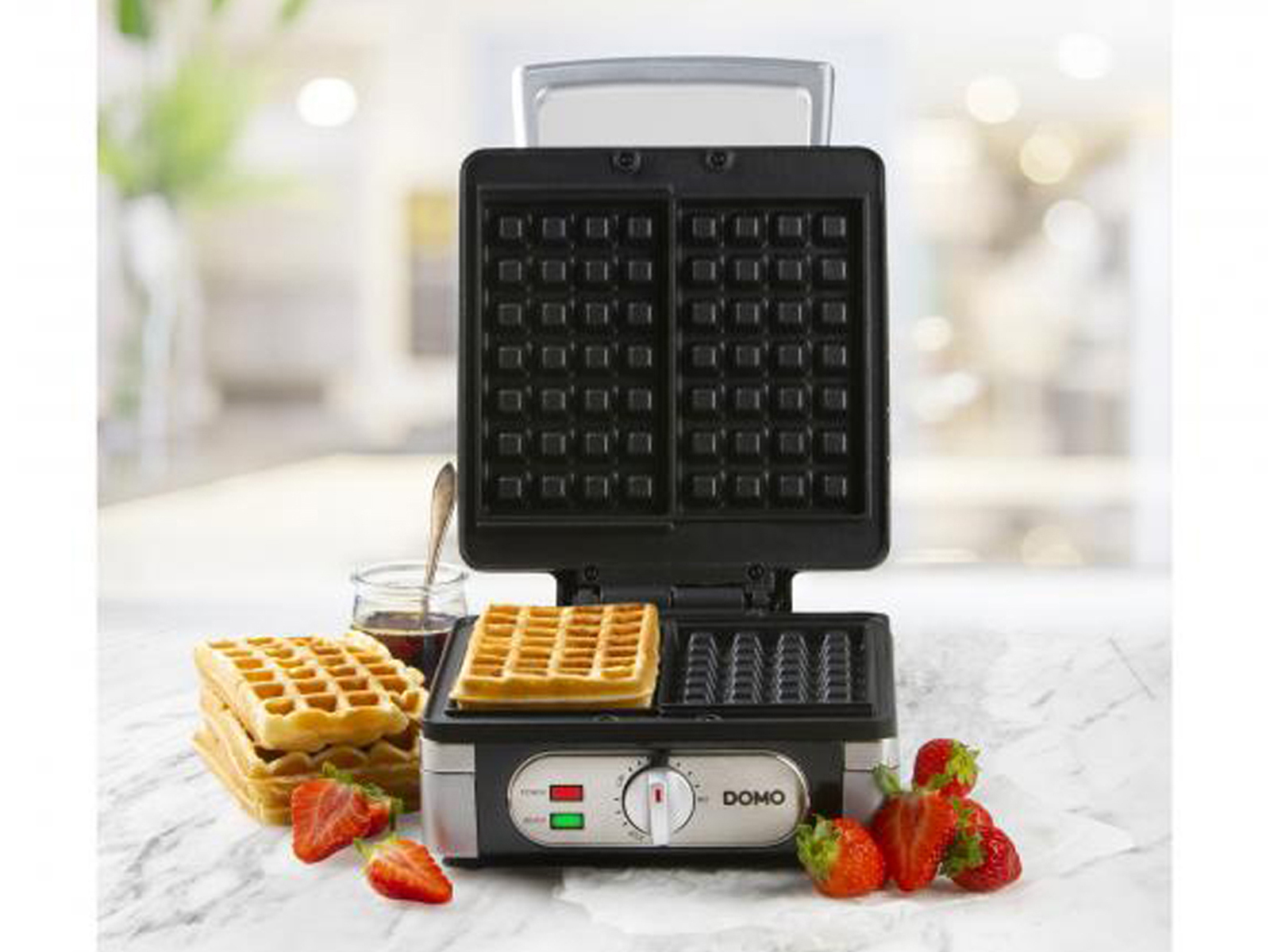 Waffeleisen mit Waffeln, Sirup und Erdbeeren.