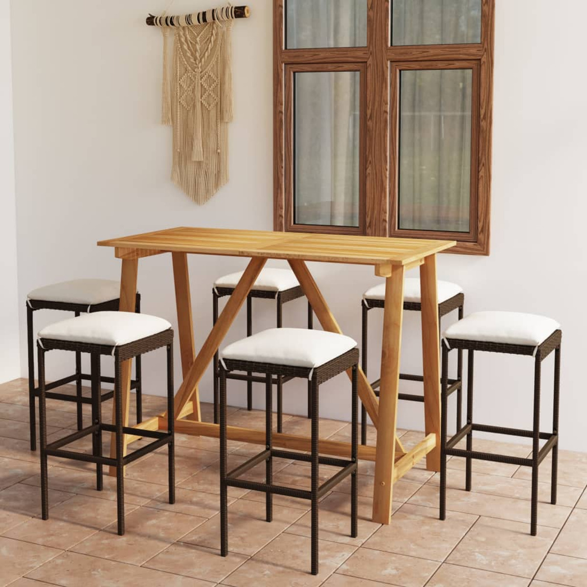 Outdoor-Bar-Set: Holztisch und sechs Hocker mit Kissen, unter einem Fenster, Makramee-Dekor an der Wand.