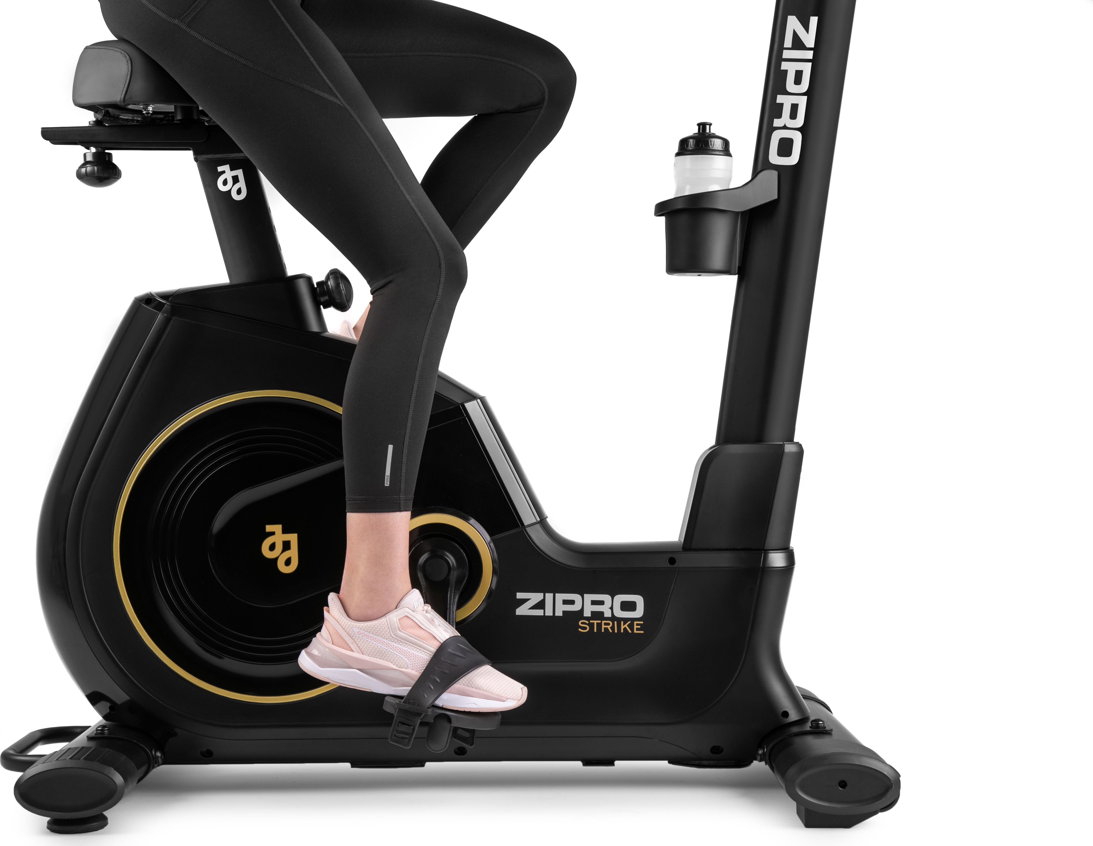 Eine Person benutzt ein stationäres Fahrrad in Schwarz und Gold. Sie tragen schwarze Leggings und rosa Schuhe.