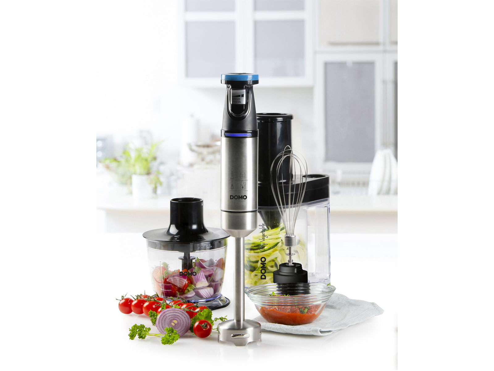 Mixer mit verschiedenen Aufsätzen. Der Mixer steht auf einer weißen Oberfläche, mit Zutaten. Weißer Hintergrund.
