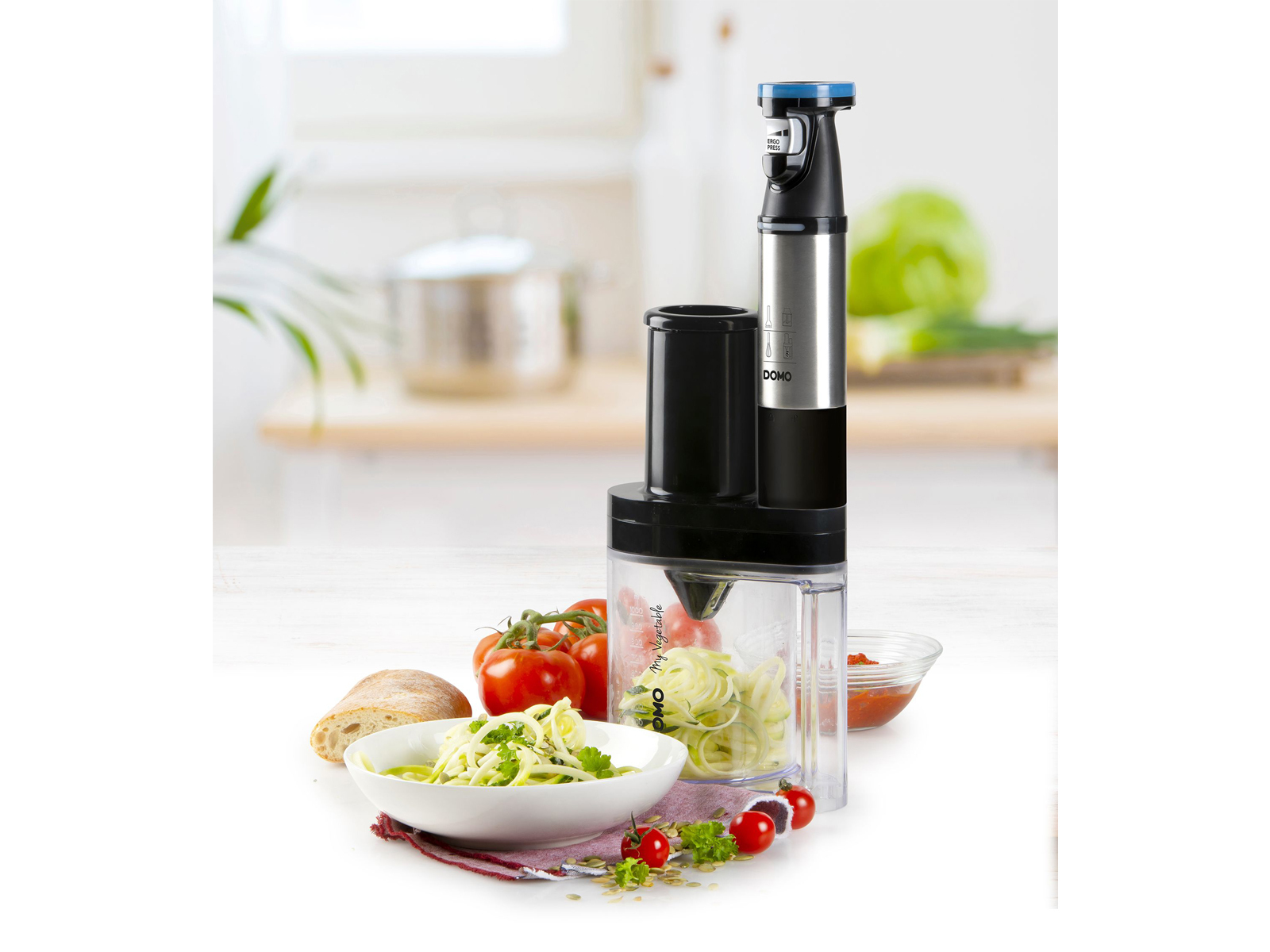 Küchenmaschine mit Zucchininudeln und Tomaten in Küchenumgebung.