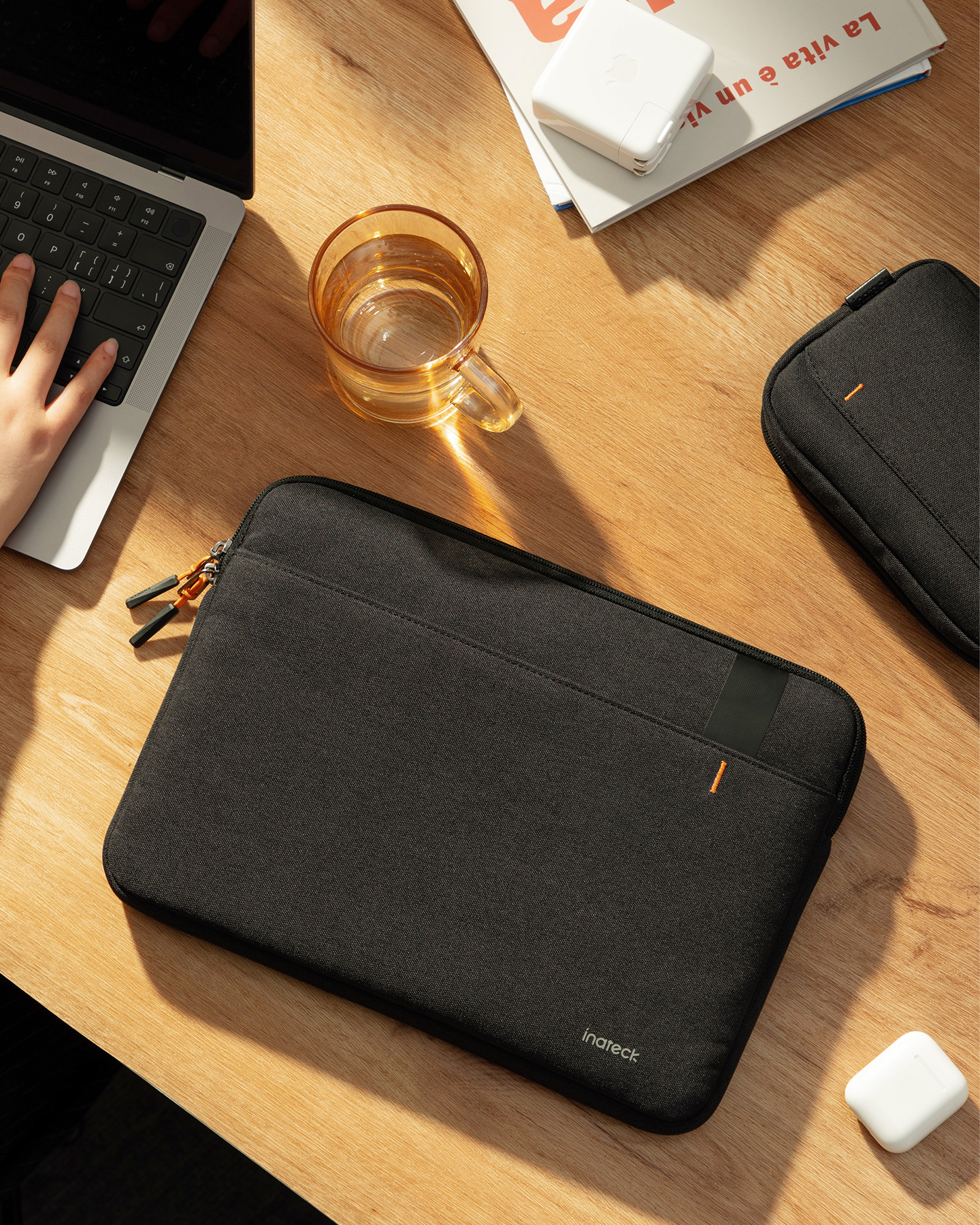 Person benutzt Laptop mit schwarzer Hülle, Kaffeetasse und Zubehör auf Holzschreibtisch.