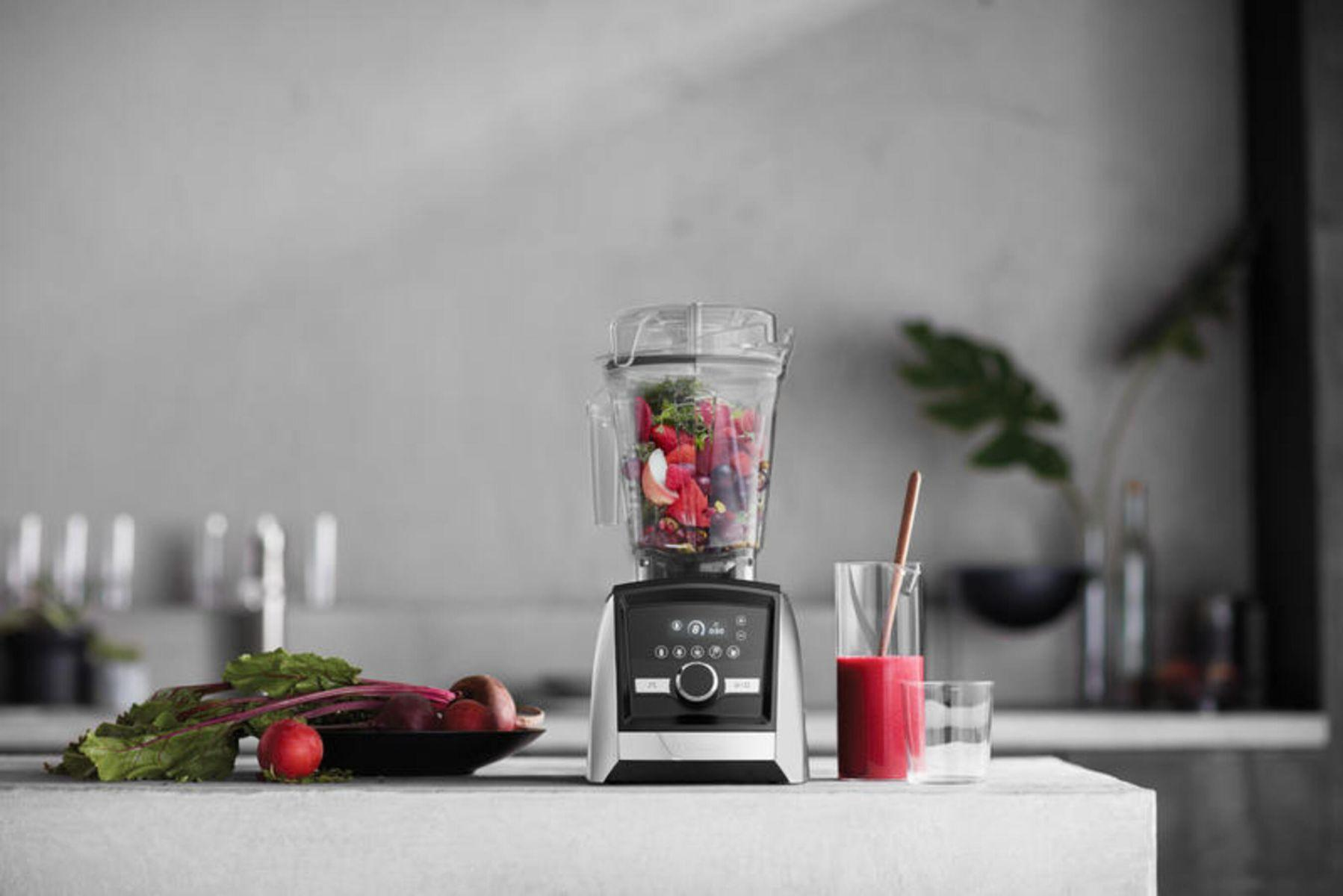 Mixer mit Zutaten. Ein Glas Saft und Gemüse stehen auf einer weißen Theke.