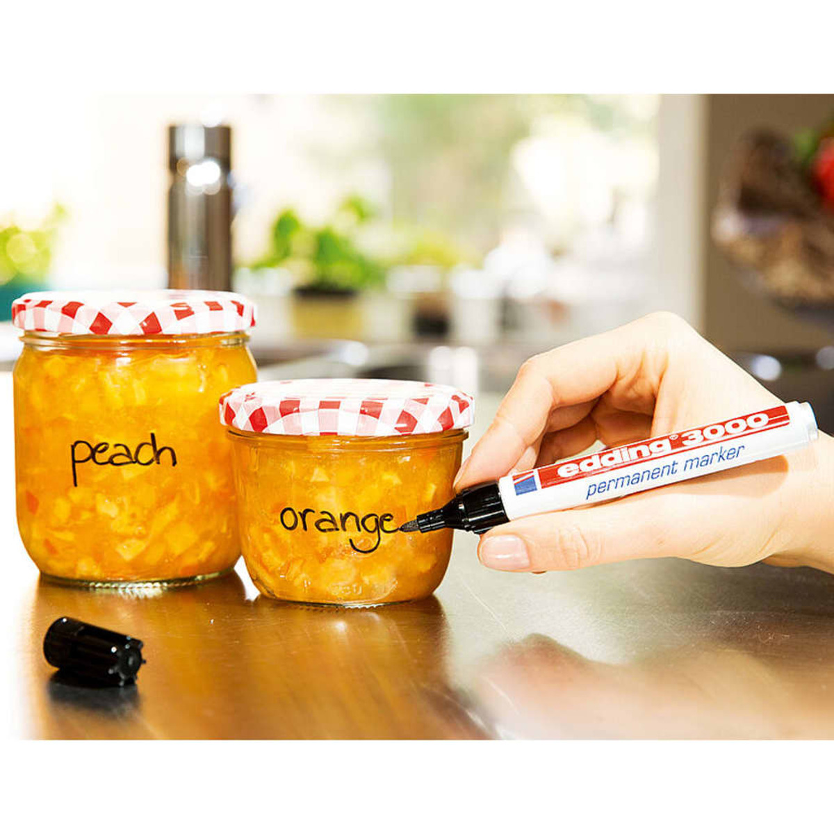 Gläser mit Pfirsich- und Orangenmarmelade werden von einer Hand mit einem schwarzen Marker beschriftet.