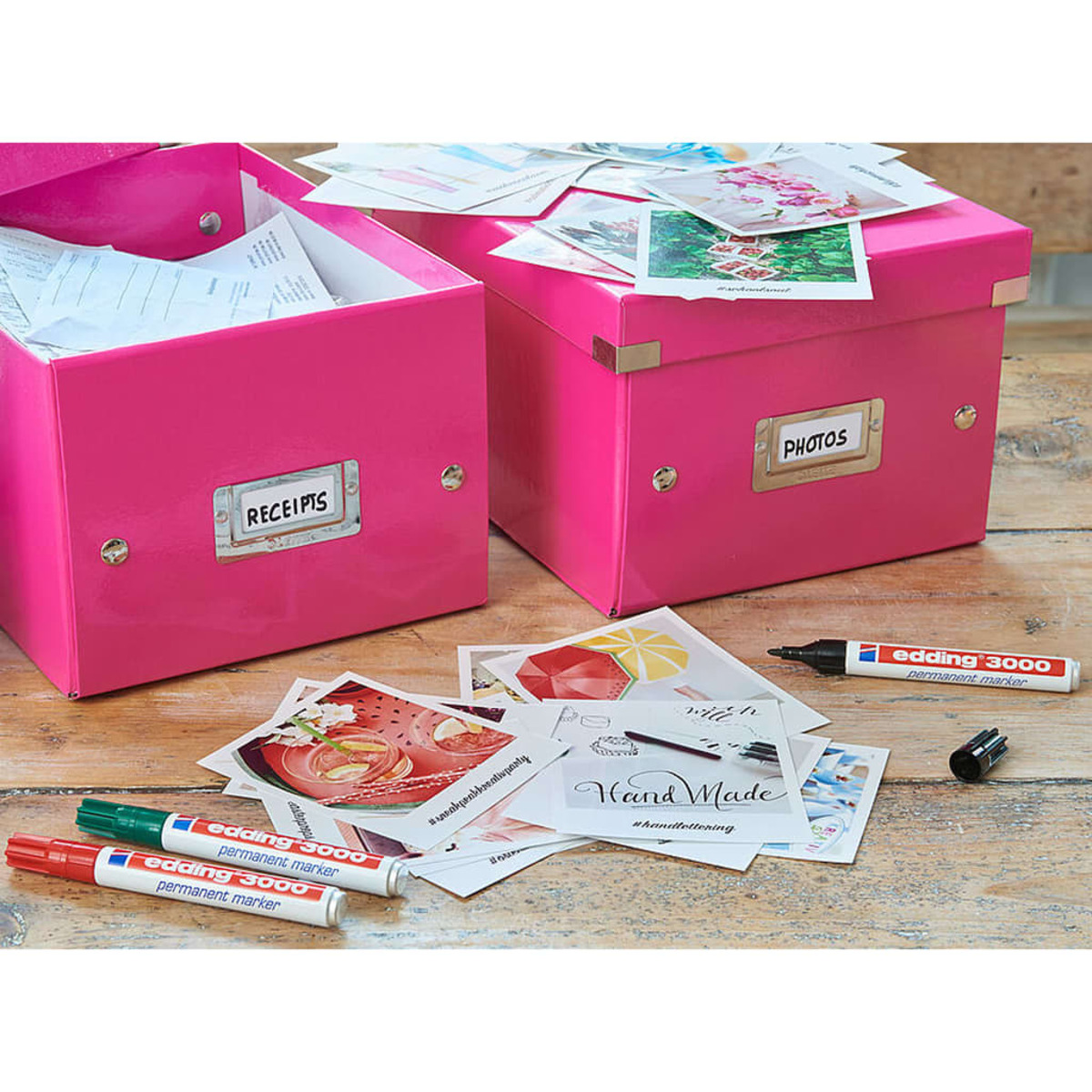 Zwei rosa Boxen mit den Aufschriften 'RECEIPTS' und 'PHOTOS' mit Schreibwaren und Markern auf Holz.
