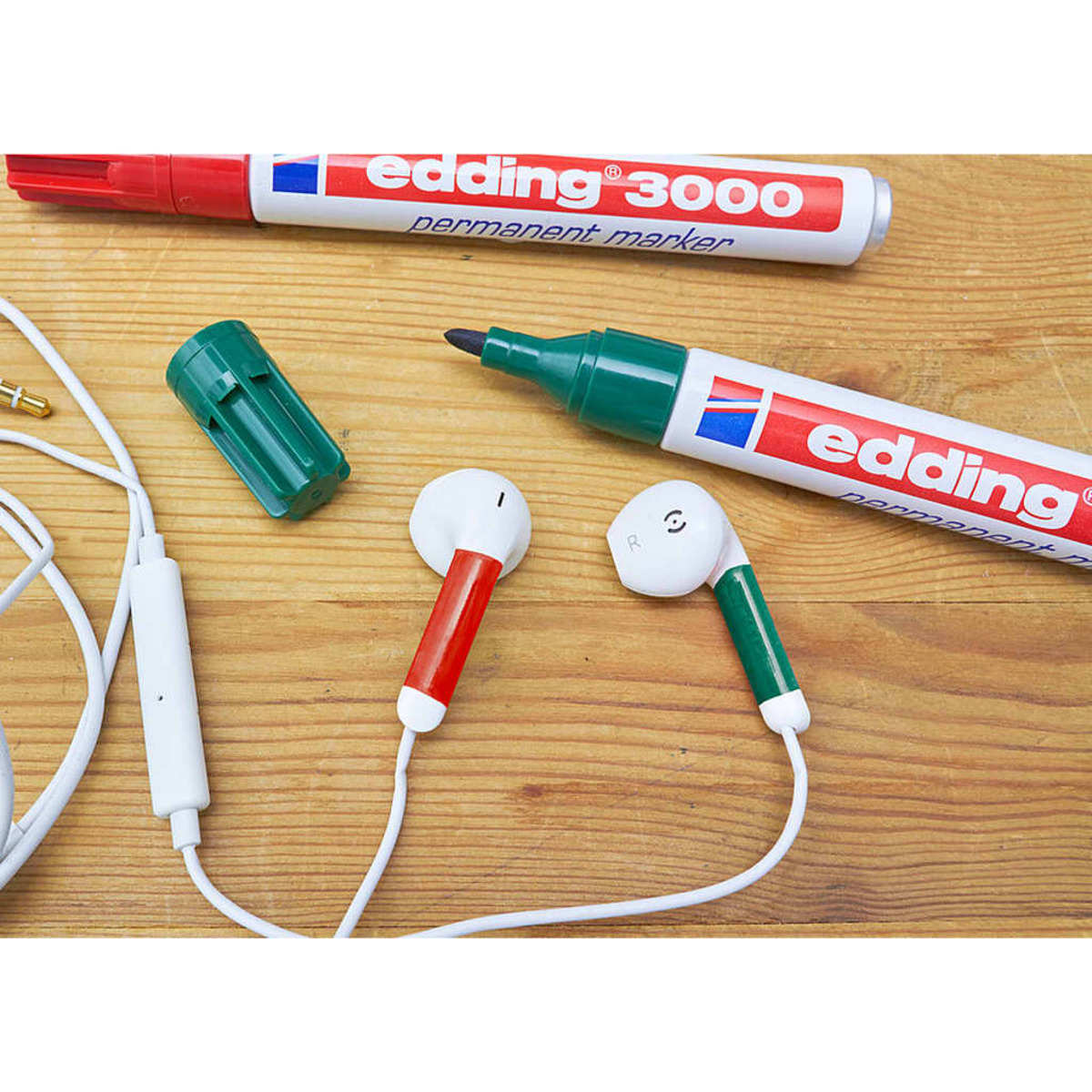 Ohrhörer, ein roter Marker und ein grüner Marker auf Holz. Weißes Kabel.