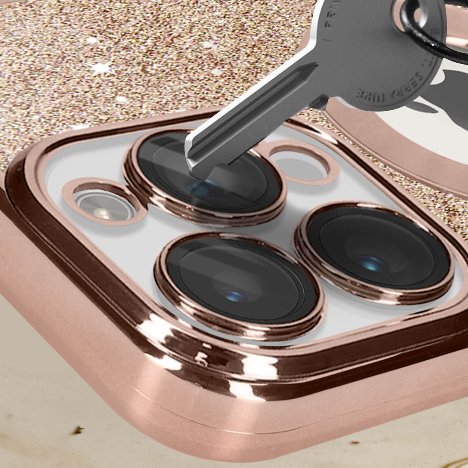 Primo piano di una custodia per telefono con una chiave accanto alle lenti della fotocamera. Oro rosa con glitter. Sfondo bianco.