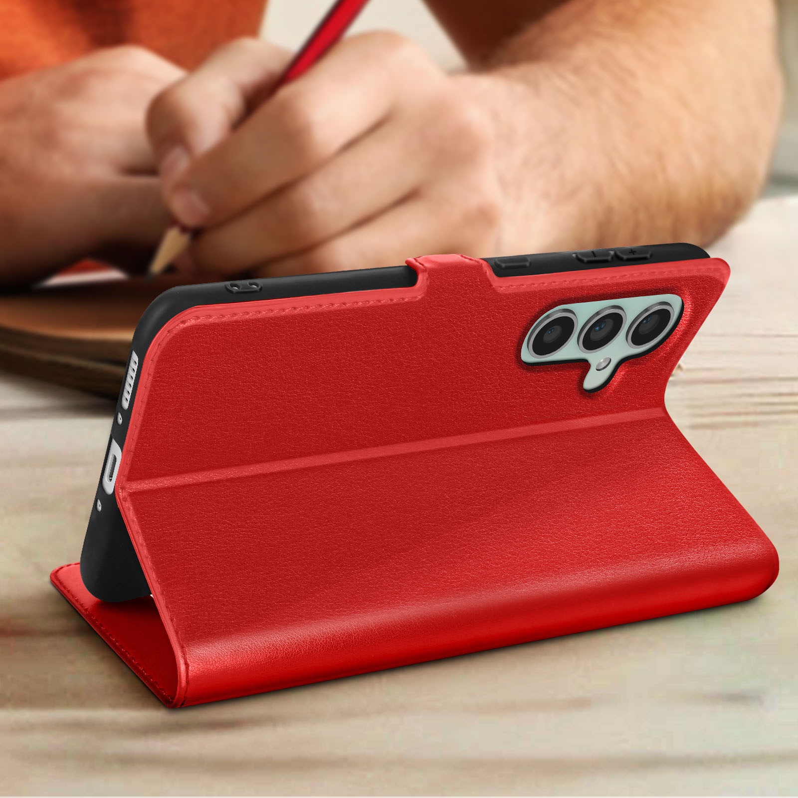 Custodia per telefono in pelle rossa con un telefono all'interno e mani di una persona che tiene una matita.