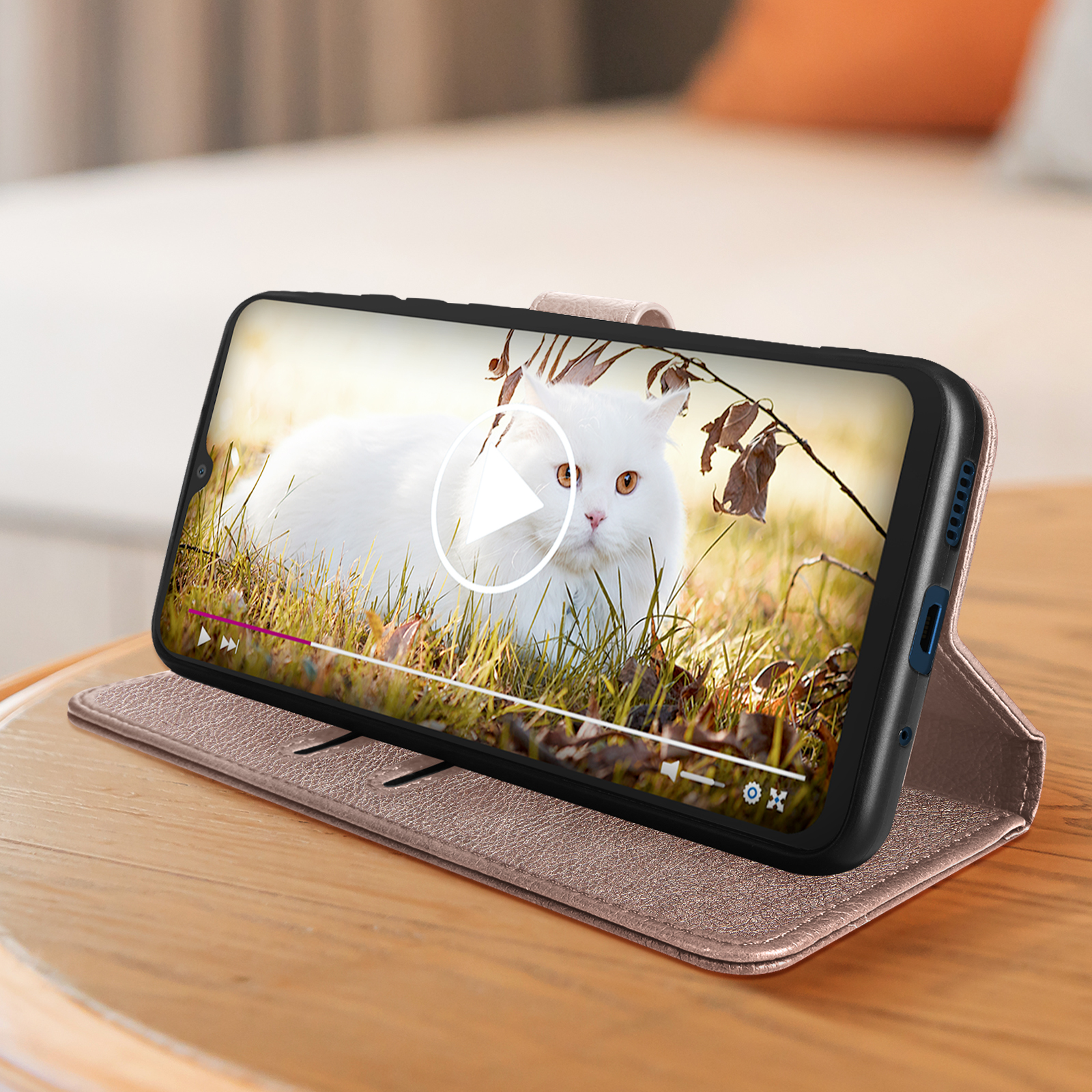 Telefono su custodia marrone, riproduce video di gatto bianco. Tavolo in legno.